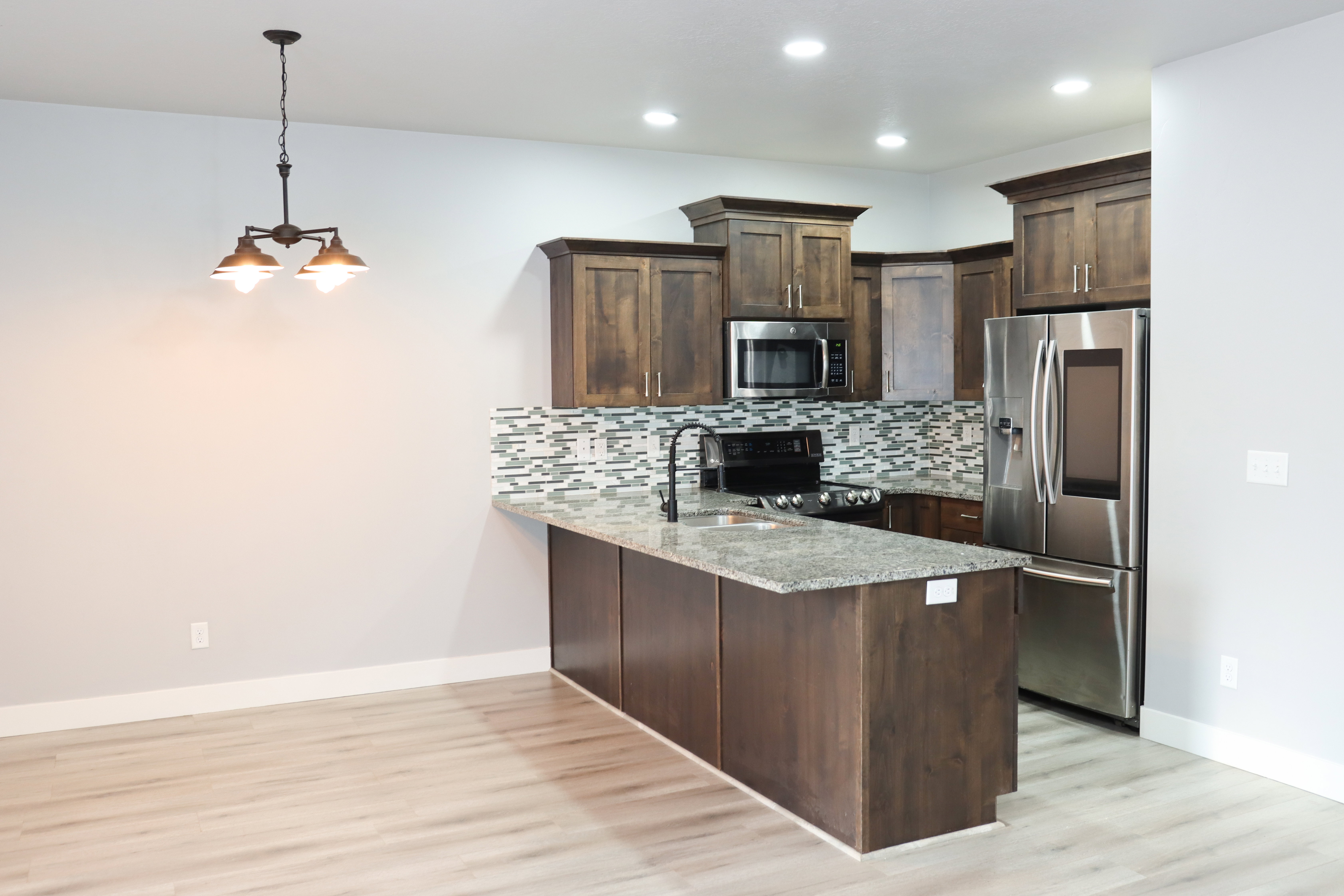 Kitchen featuring wood-finish cabinetry, stainless steel appliances, a multi-tone tile backsplash, granite countertops, and recessed lighting