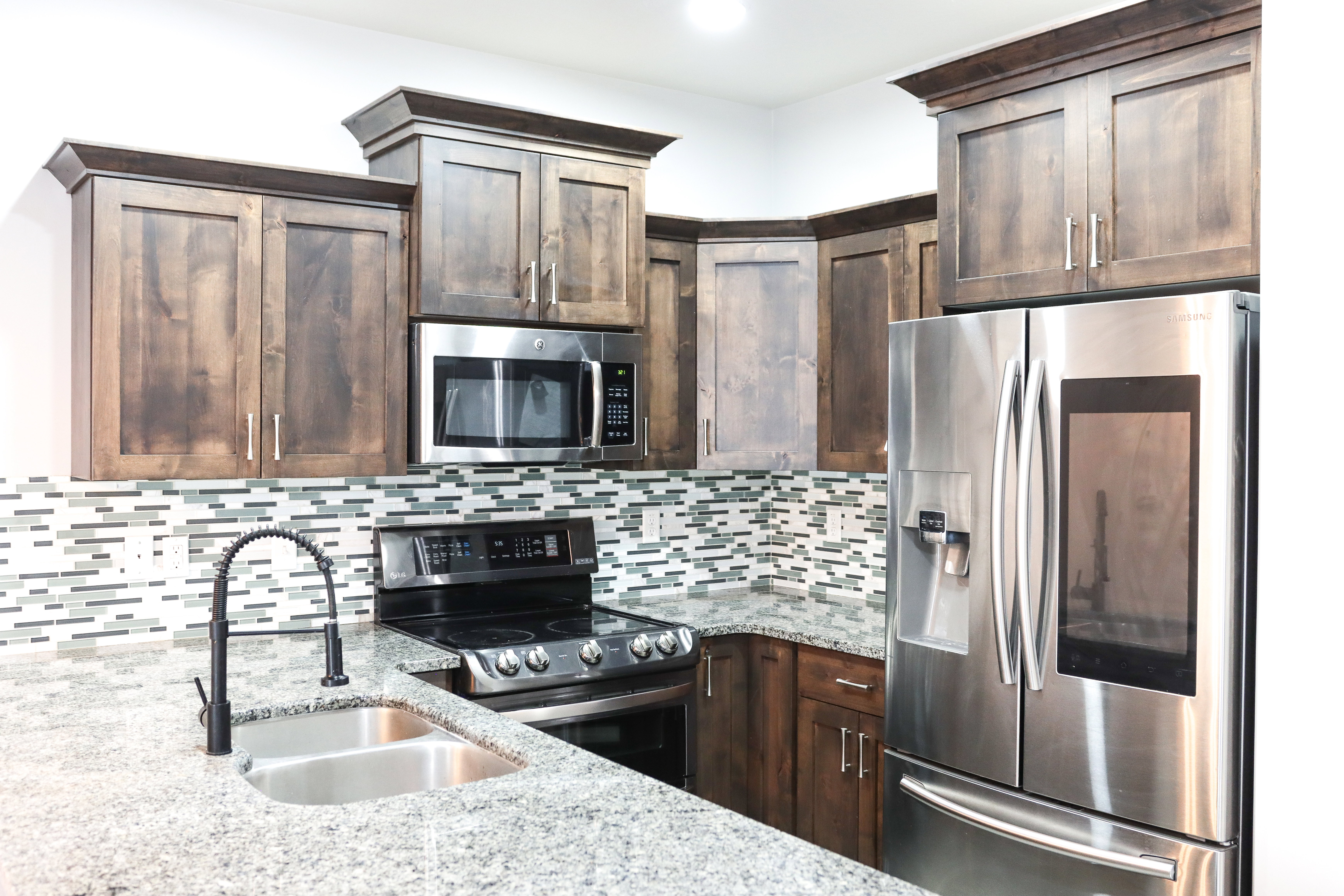Kitchen featuring wood-finish cabinetry, stainless steel appliances, speckled stone countertops, and a mosaic tile backsplash