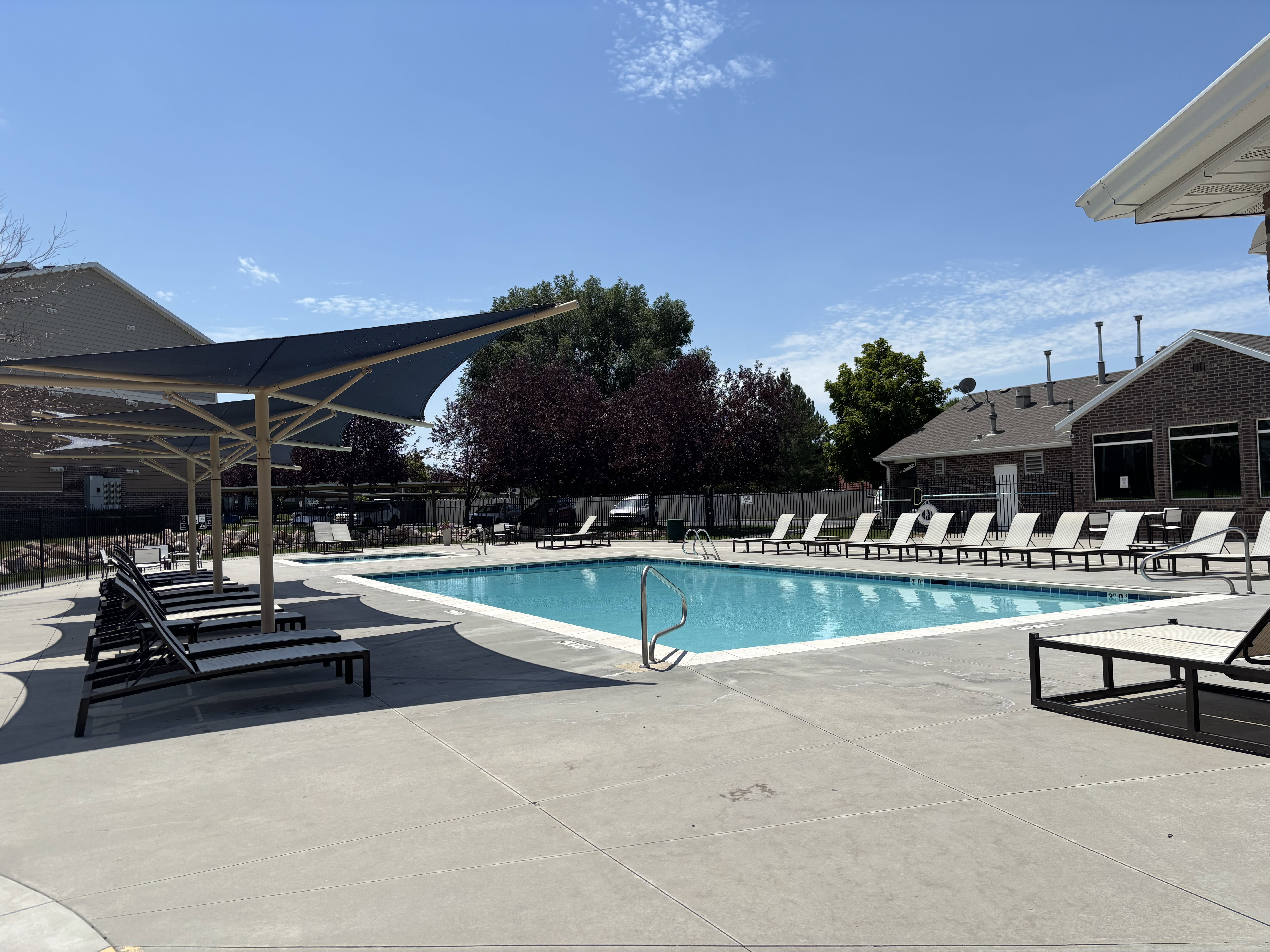 Swimming pool with concrete decking, multiple lounge chairs, and shade structures