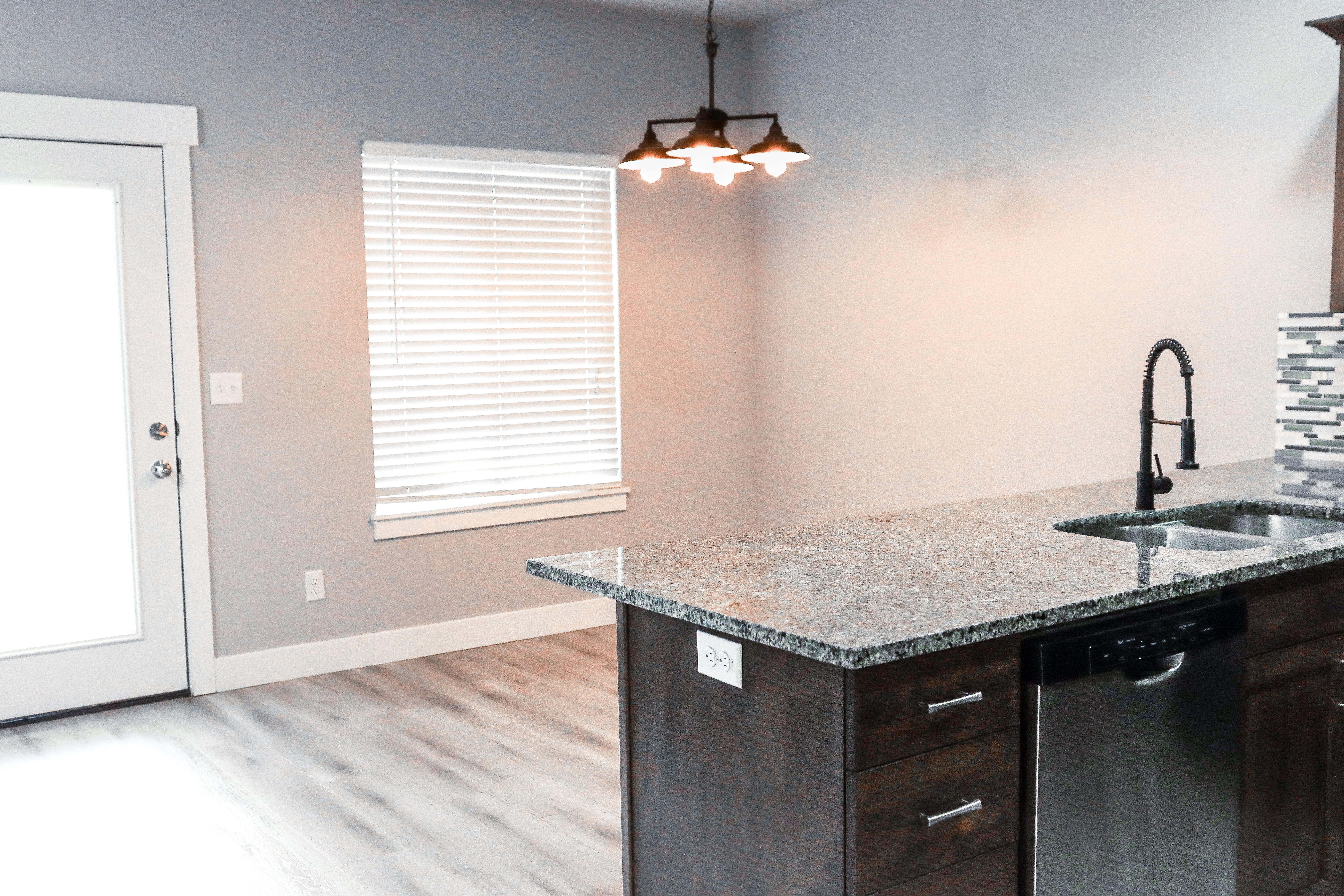 Kitchen island featuring a granite countertop, stainless steel sink with a matte black faucet, and integrated dishwasher