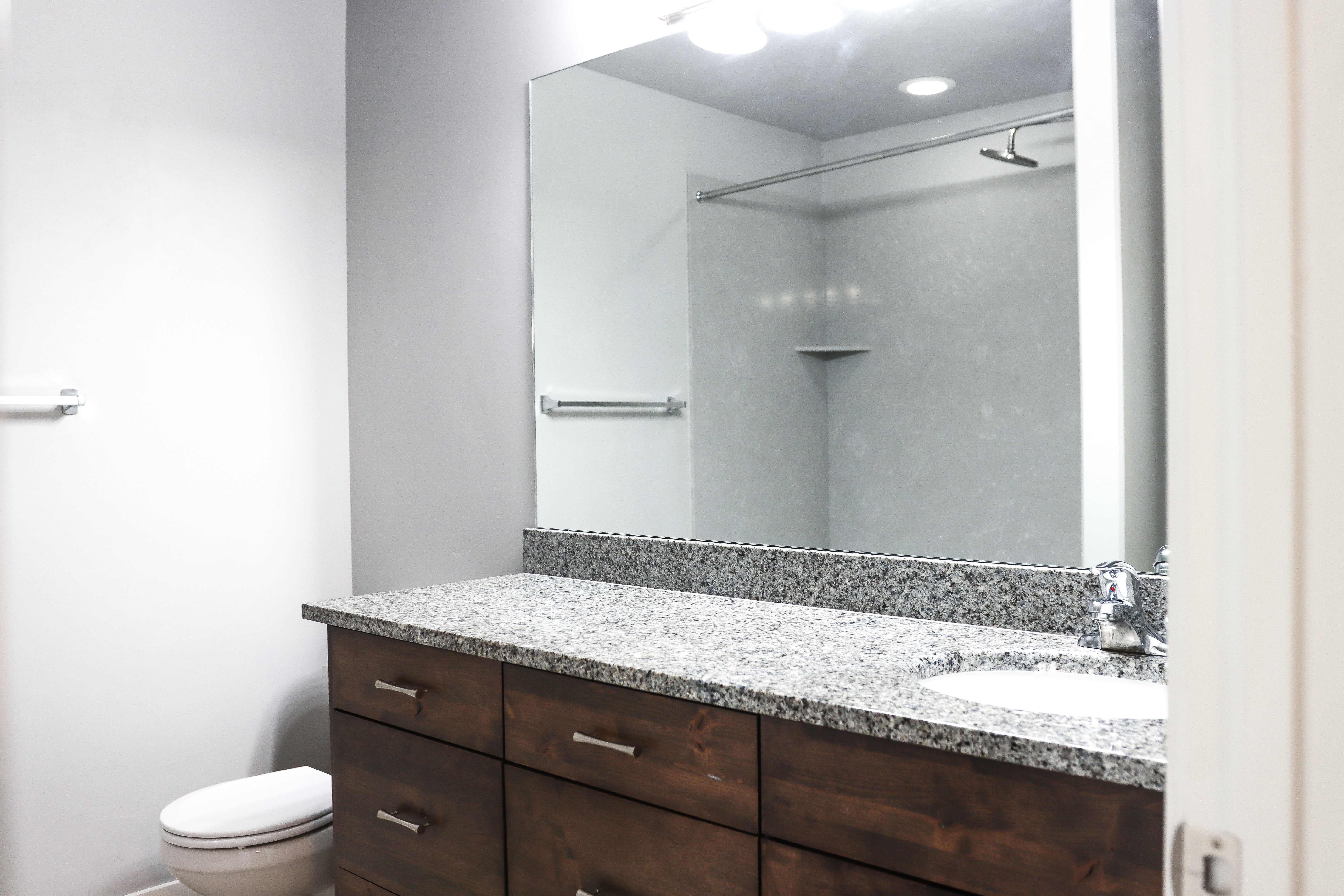 Bathroom featuring a dark wood-finish vanity with chrome hardware, a light-toned stone countertop, and an integrated white sink