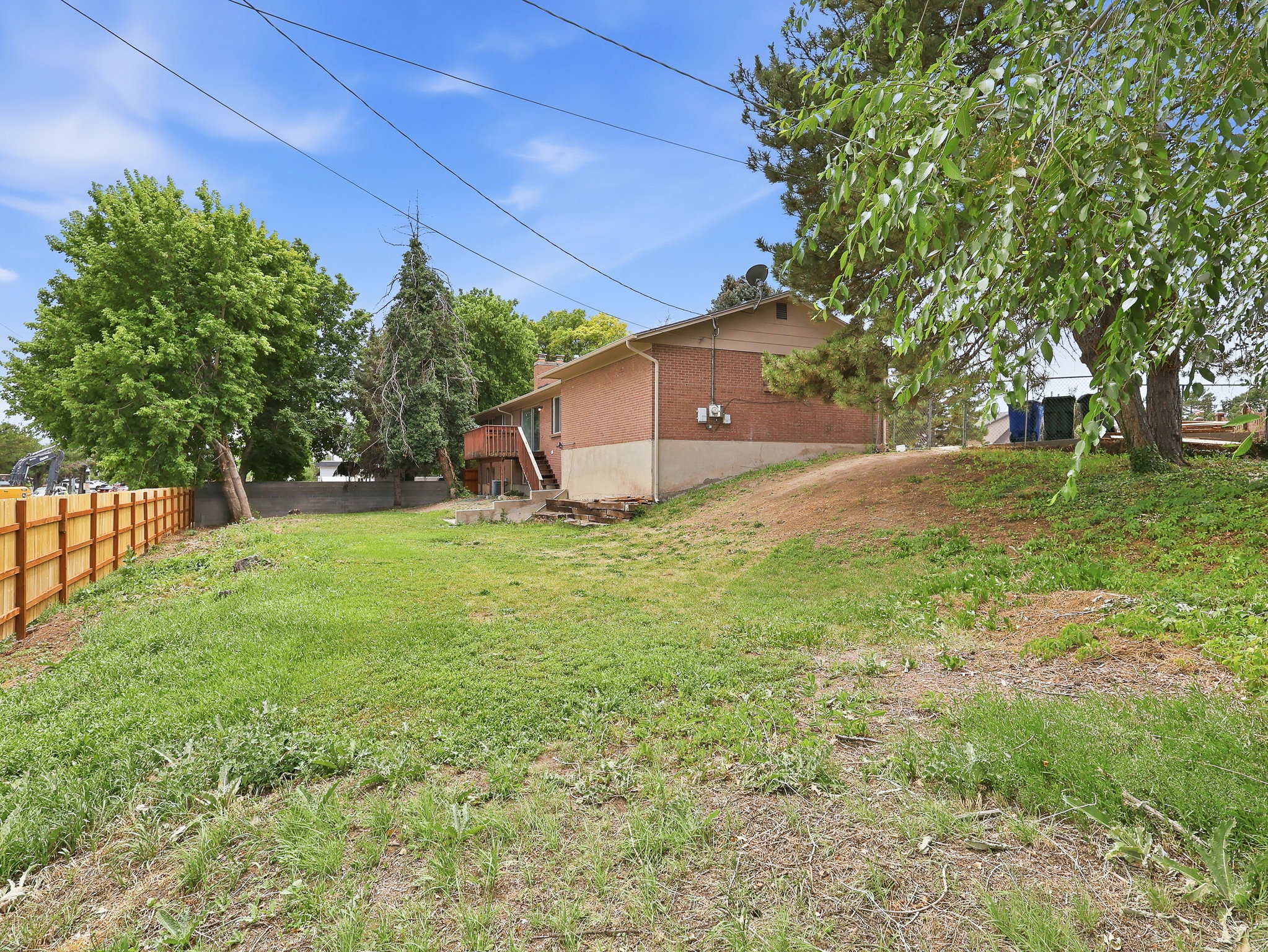 Expansive sloped backyard featuring a wood privacy fence and mature trees