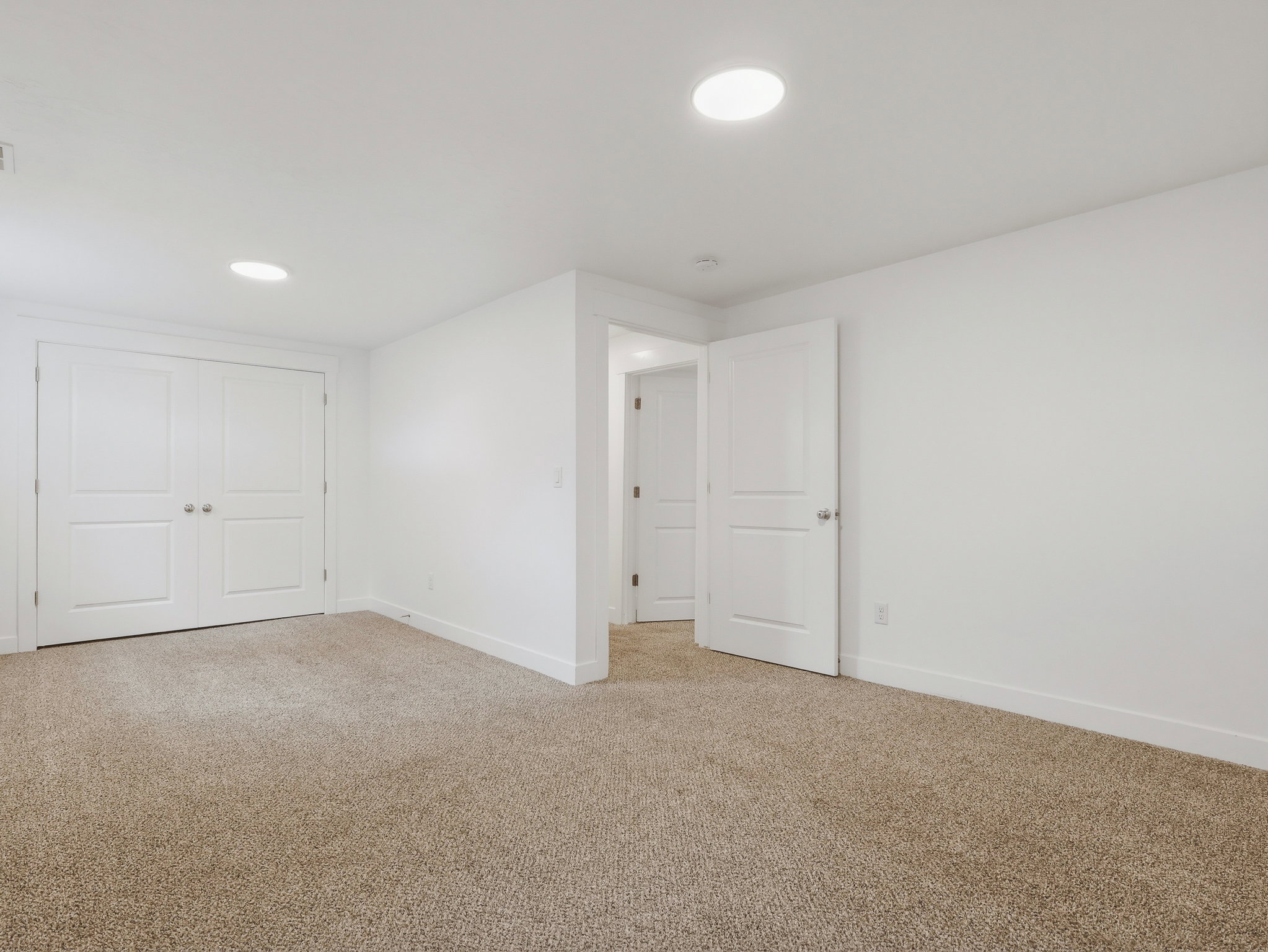 Carpeted room featuring recessed ceiling lighting, a pair of paneled bifold doors, and a single paneled door providing access to an additional interior space