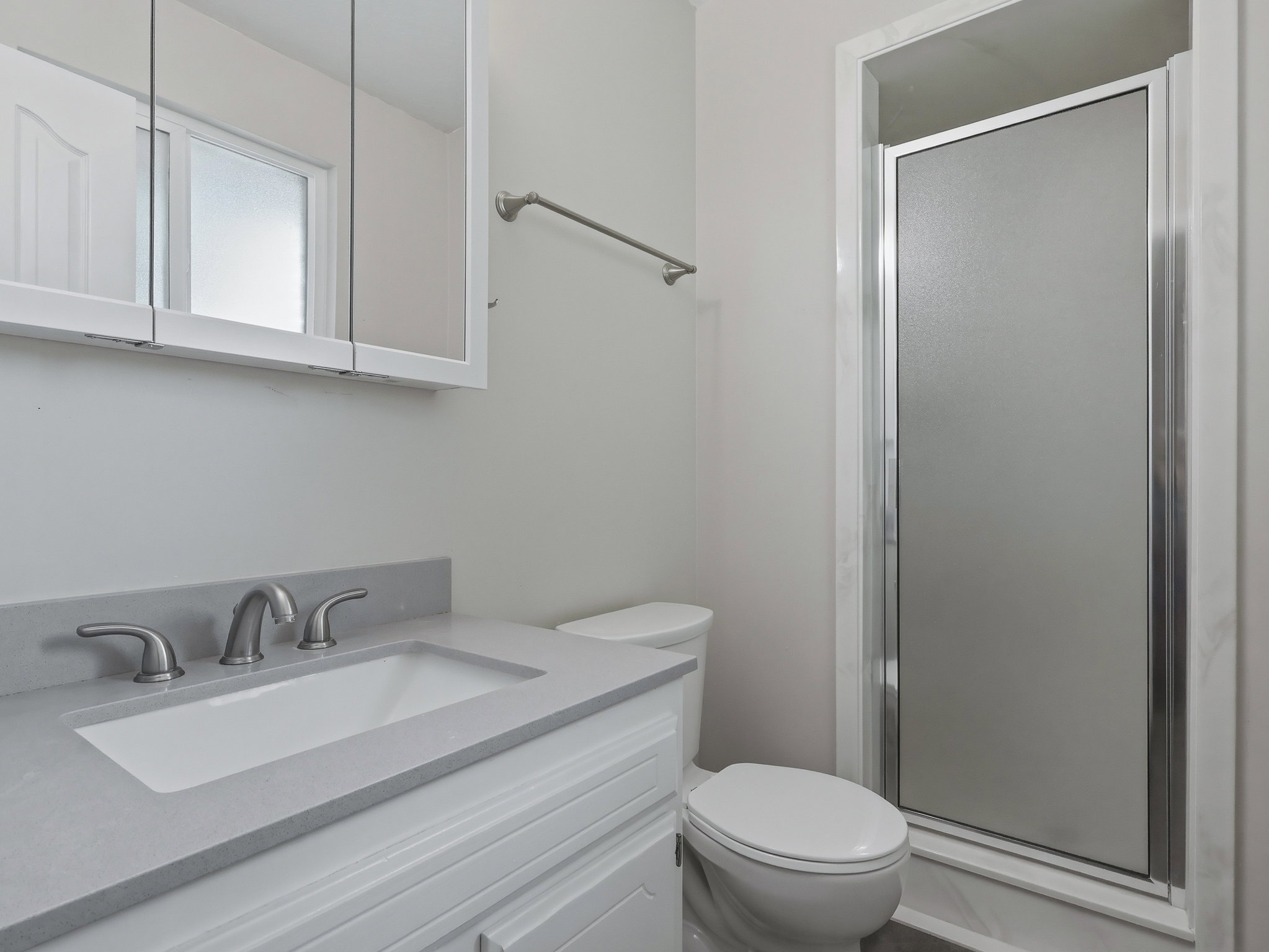 Bathroom featuring a light-colored vanity with an integrated sink, a matching countertop, a three-piece faucet, and a frameless shower enclosure with a frosted glass door