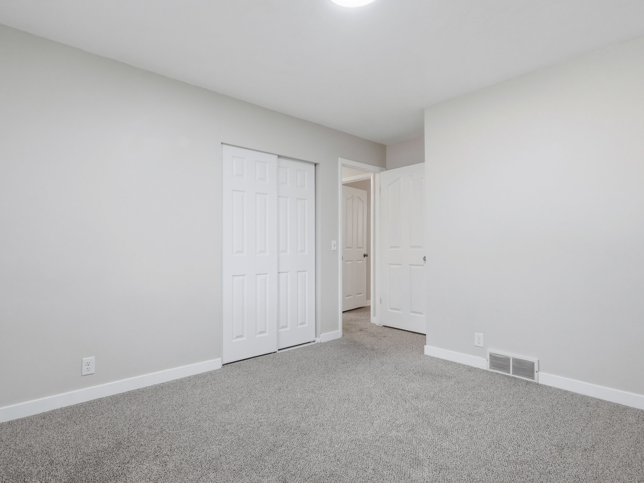 Carpeted room featuring light gray wall paint, white trim, a ceiling-mounted light fixture, sliding closet doors, and an open doorway