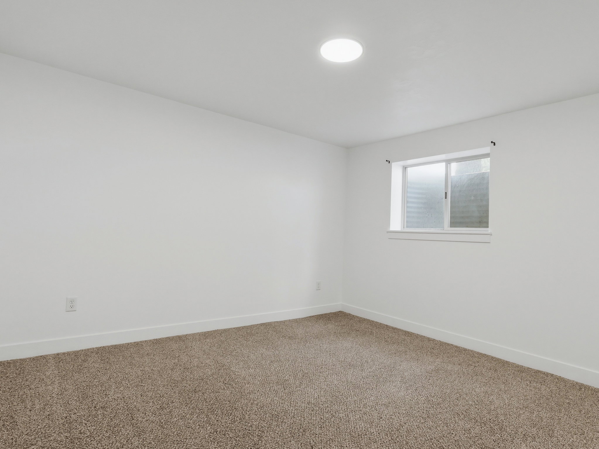 White-painted room featuring light brown carpet, a recessed ceiling light, and a single window with white trim