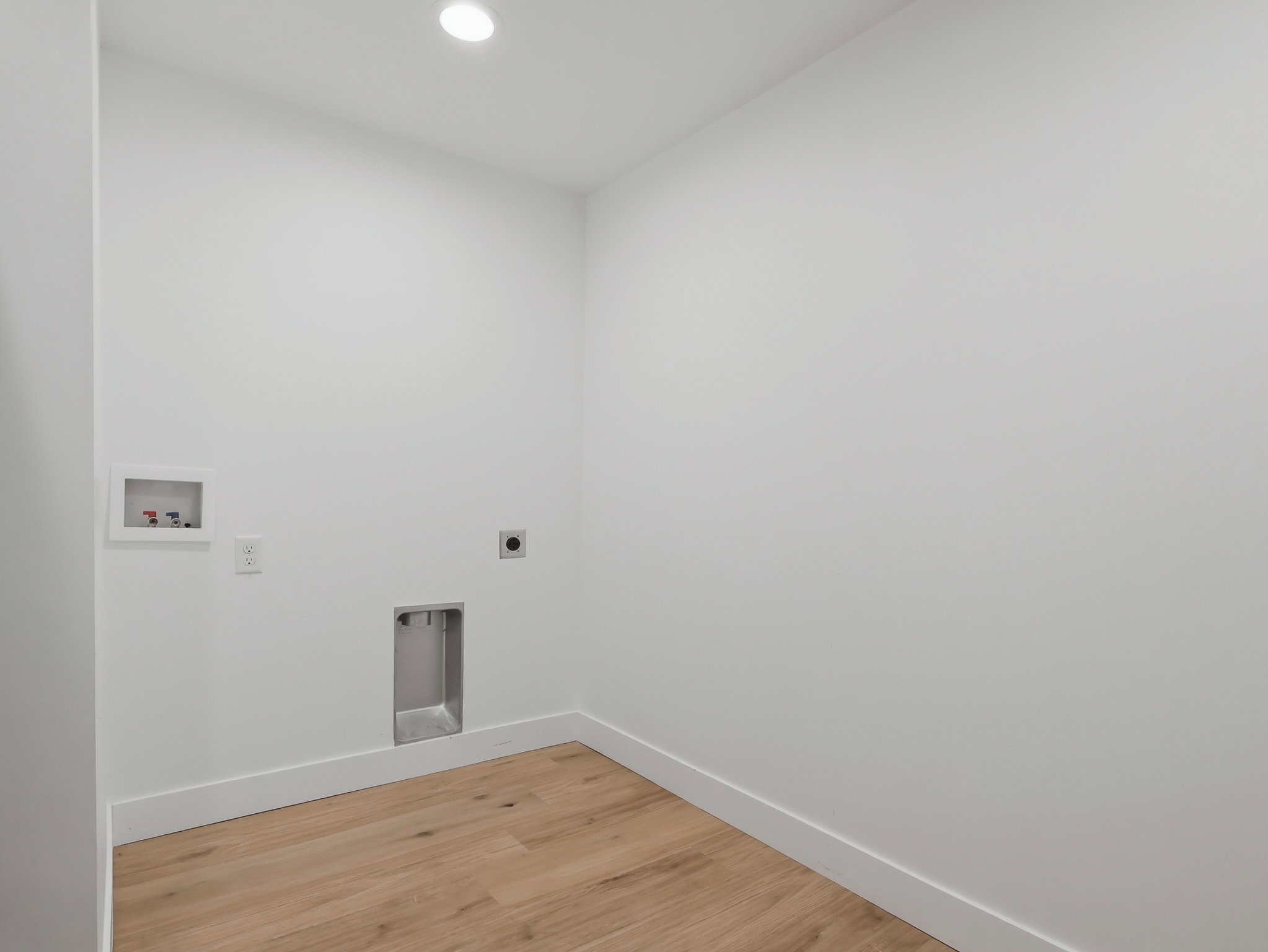 Dedicated laundry room featuring light wood-finish flooring, recessed lighting, and crisp white walls with thick baseboards