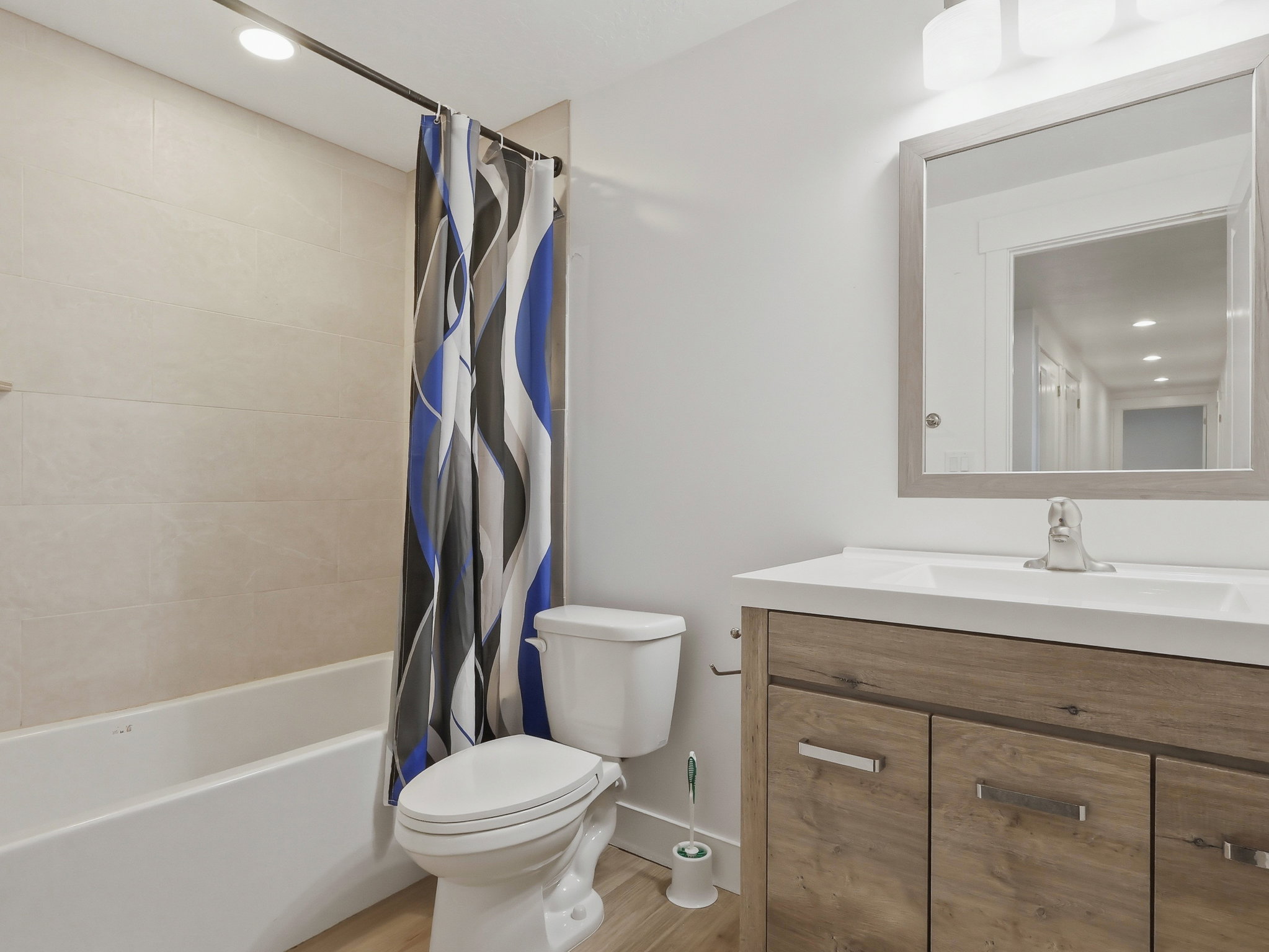 Bathroom featuring a built-in tub with tile surround, a single vanity with wood-finish cabinetry, a rectangular basin, and a framed mirror