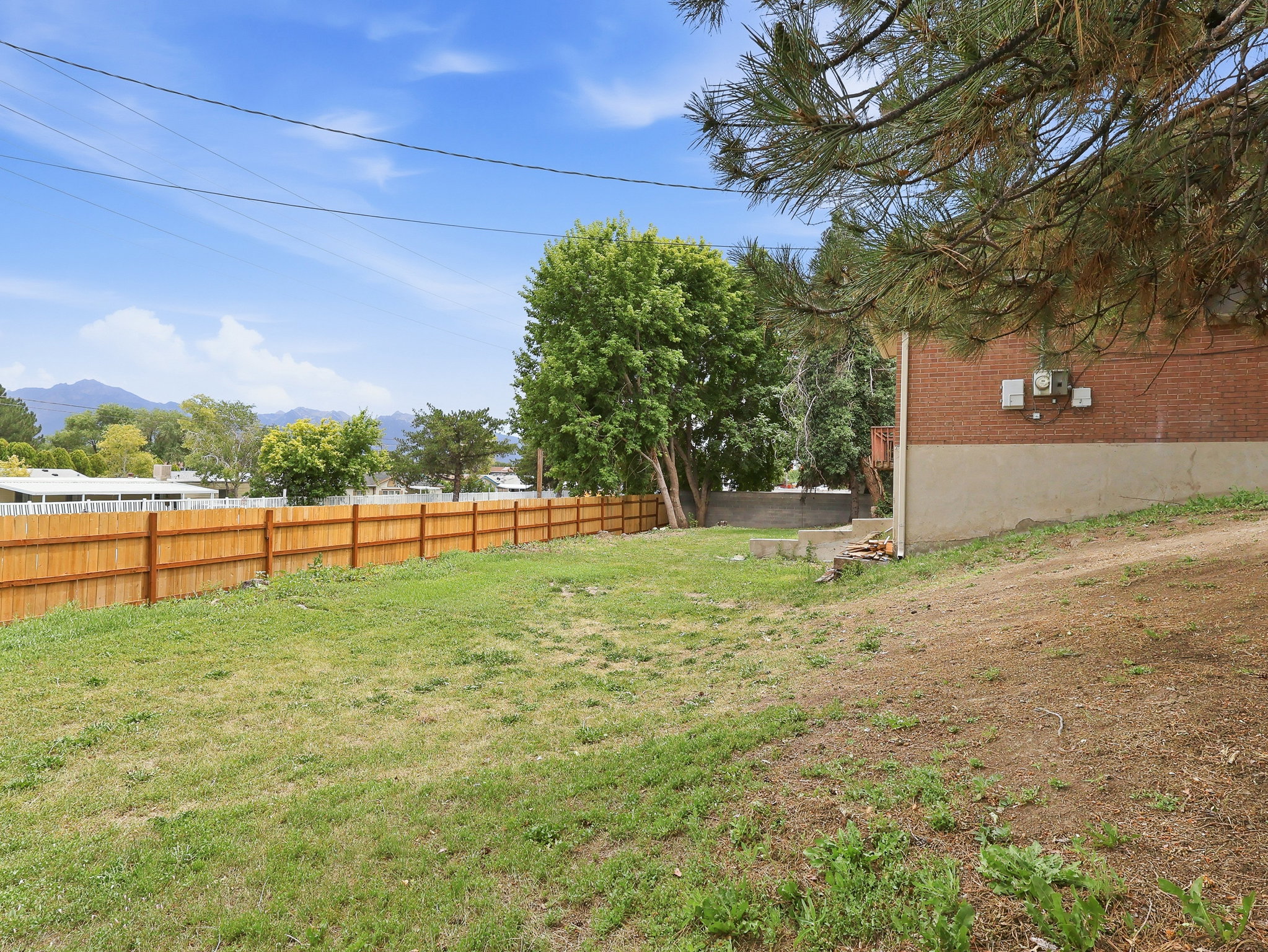 Expansive outdoor space featuring a new wood privacy fence, mature trees, and mountain scenery