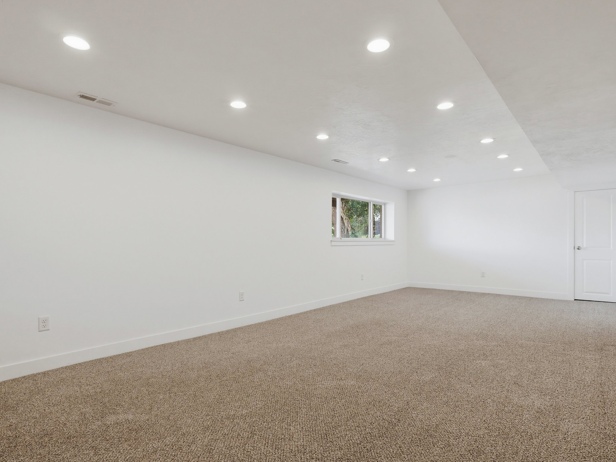 Carpeted interior space featuring recessed lighting, a white painted door, a window with white trim, and white baseboards