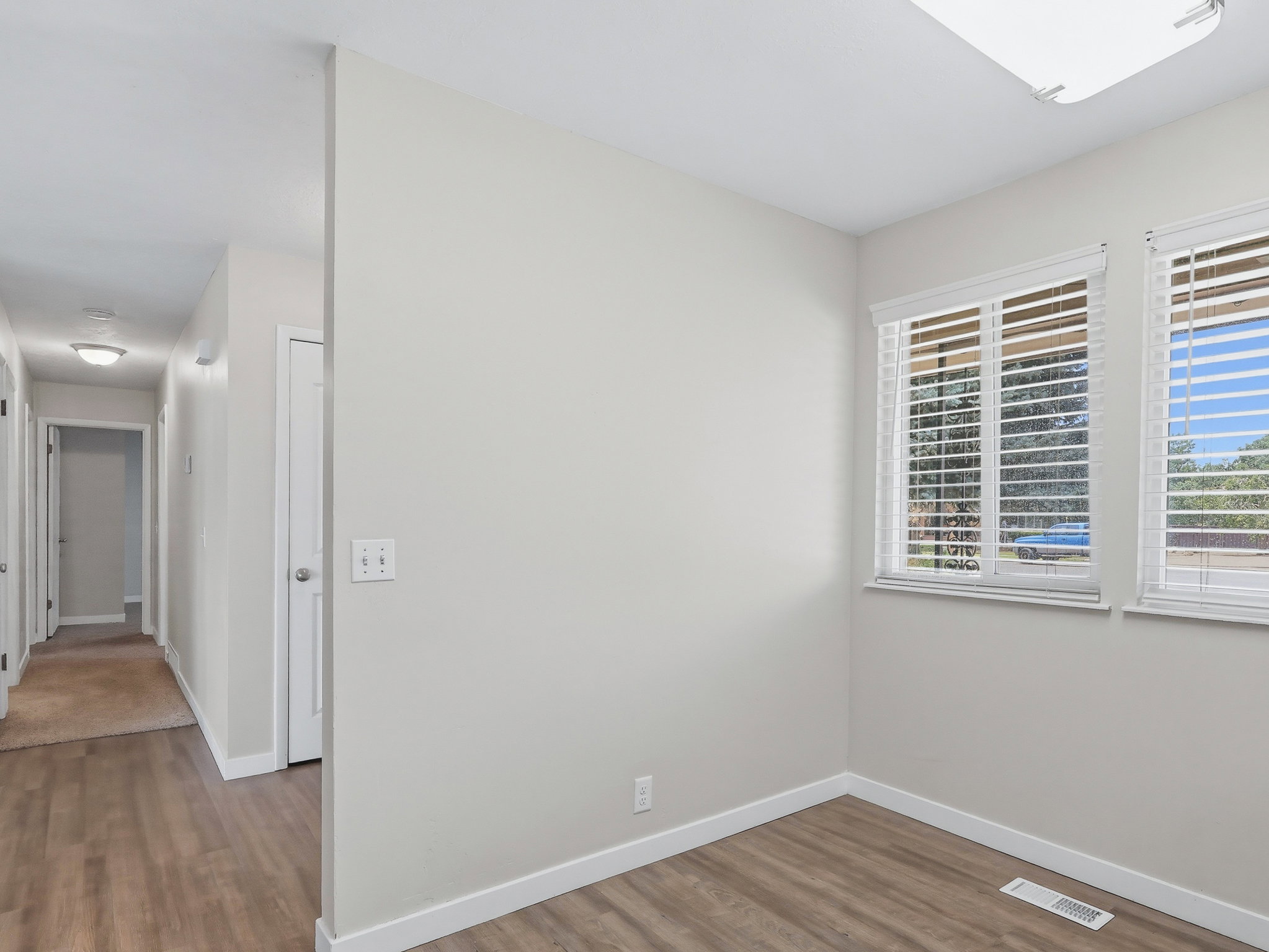 Room with wood-finish flooring, two large windows with blinds, and light-toned walls