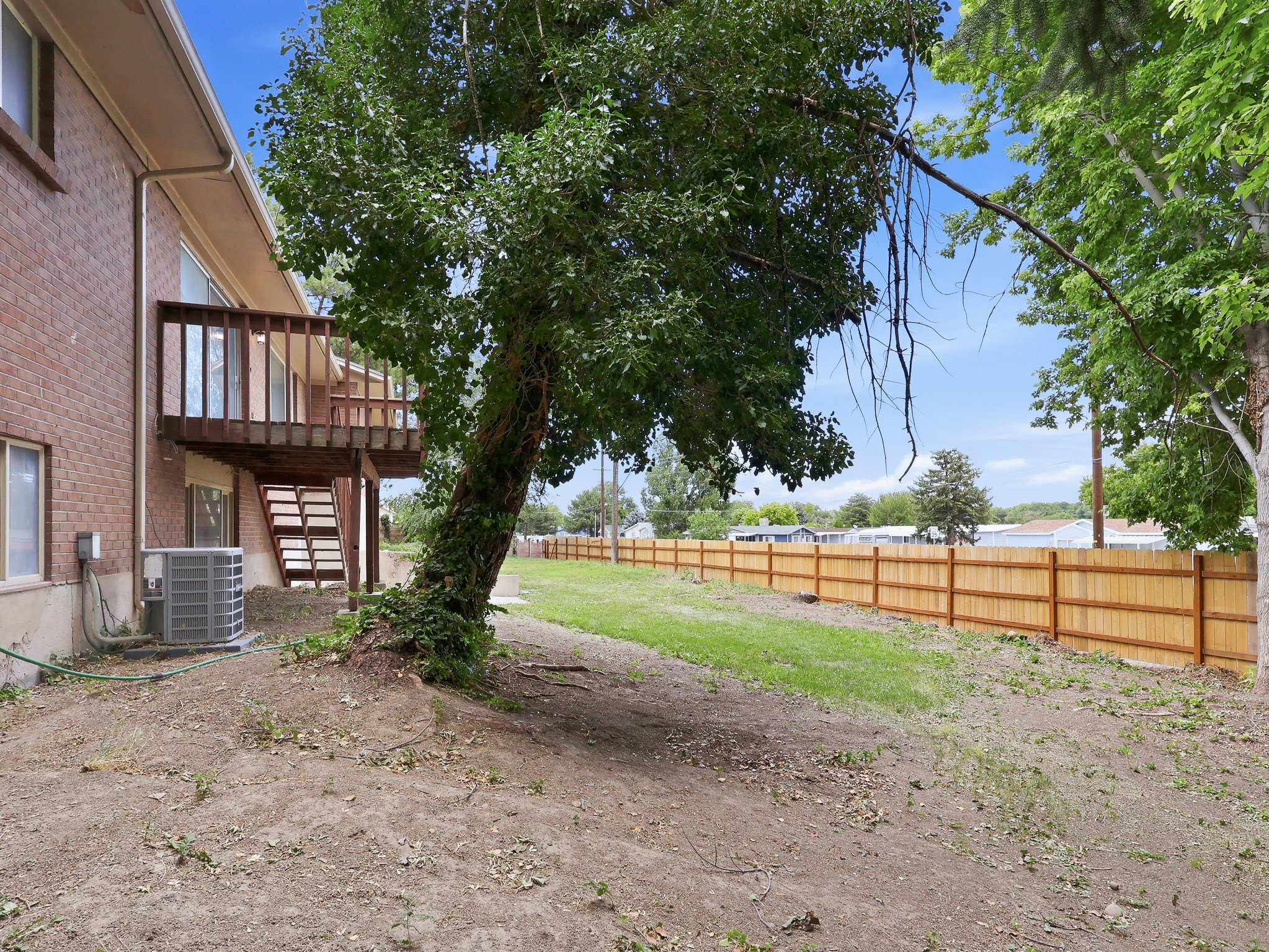 Rear exterior featuring a wood deck with stairs, a brick facade, and a private backyard with a wood fence and mature trees