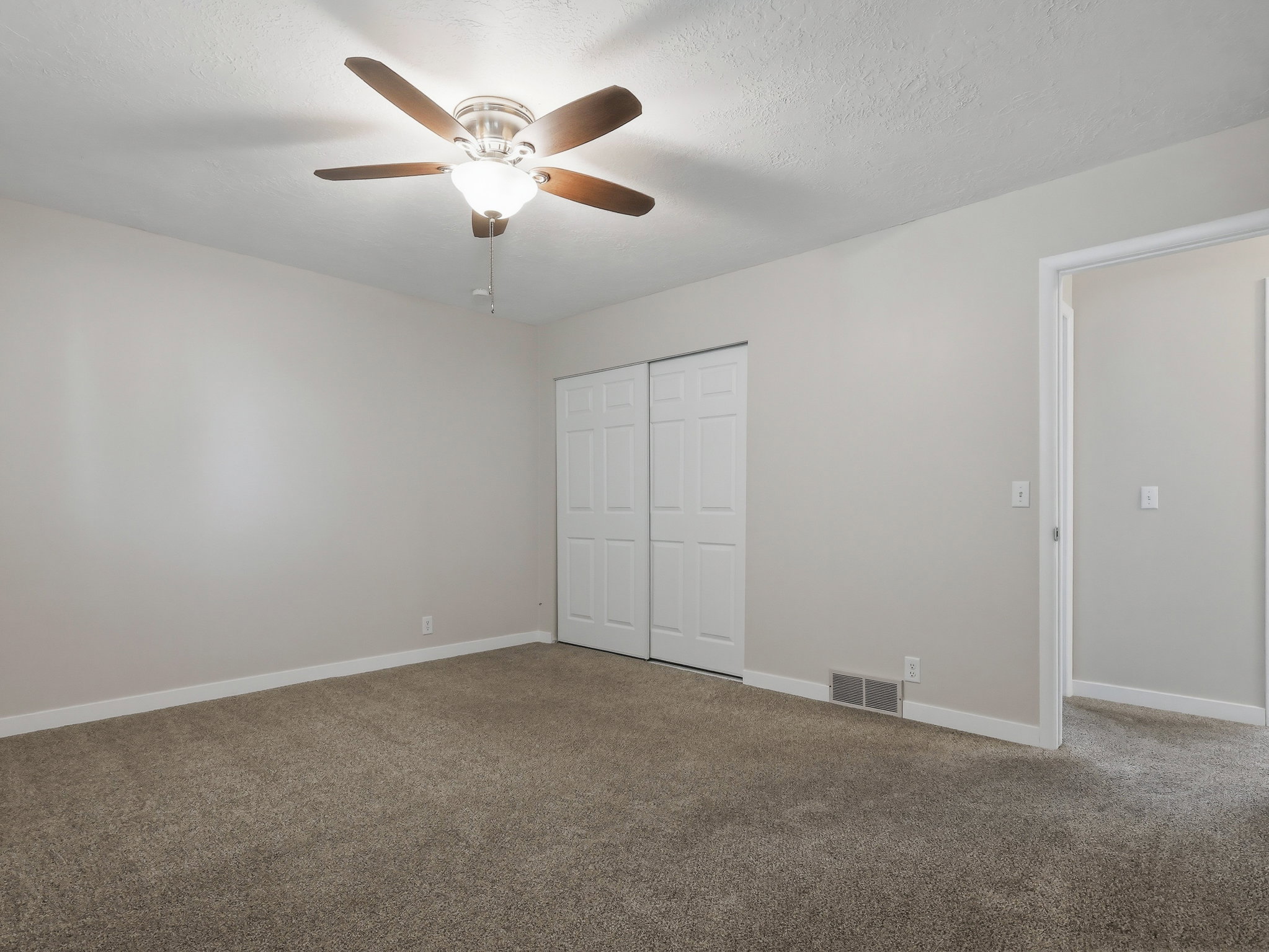 Carpeted room featuring light gray walls, a ceiling fan with light fixture, and white bi-fold closet doors