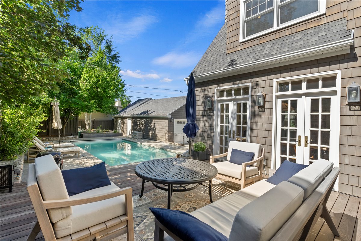 Expansive outdoor living area featuring a wood-finish deck, an inground swimming pool with stone coping, and French doors leading into the residence