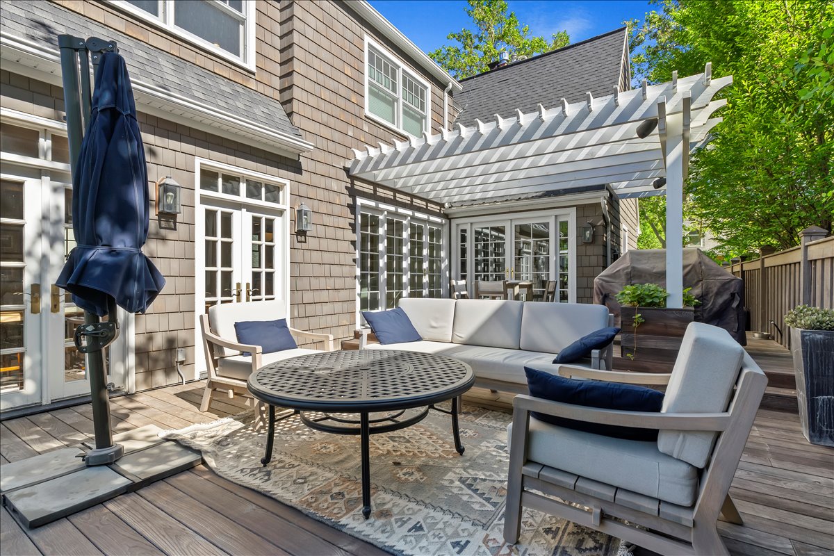 Expansive wood-finish deck with a white pergola, offering multiple sets of French doors and exterior wall sconces