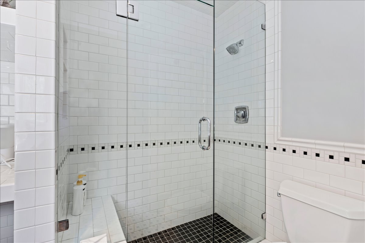 Enclosed shower with clear glass paneling featuring white subway tile walls and black mosaic tile flooring