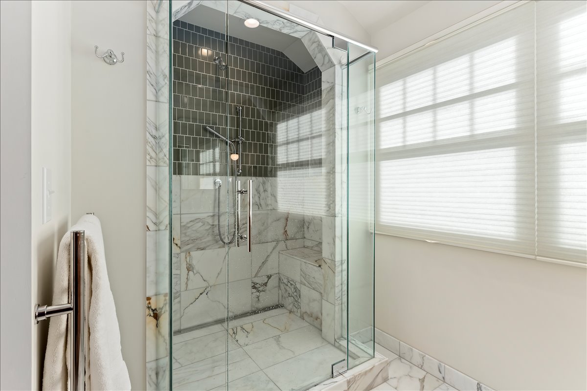 Glass-enclosed shower featuring marble-patterned tile walls, a built-in bench, and a rectangular tile accent band