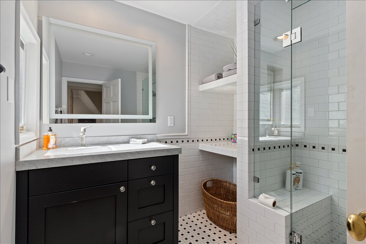 Bathroom featuring a black vanity with a white countertop and an undermount sink, a framed mirror, and a glass-enclosed shower with white subway tile and a built-in bench