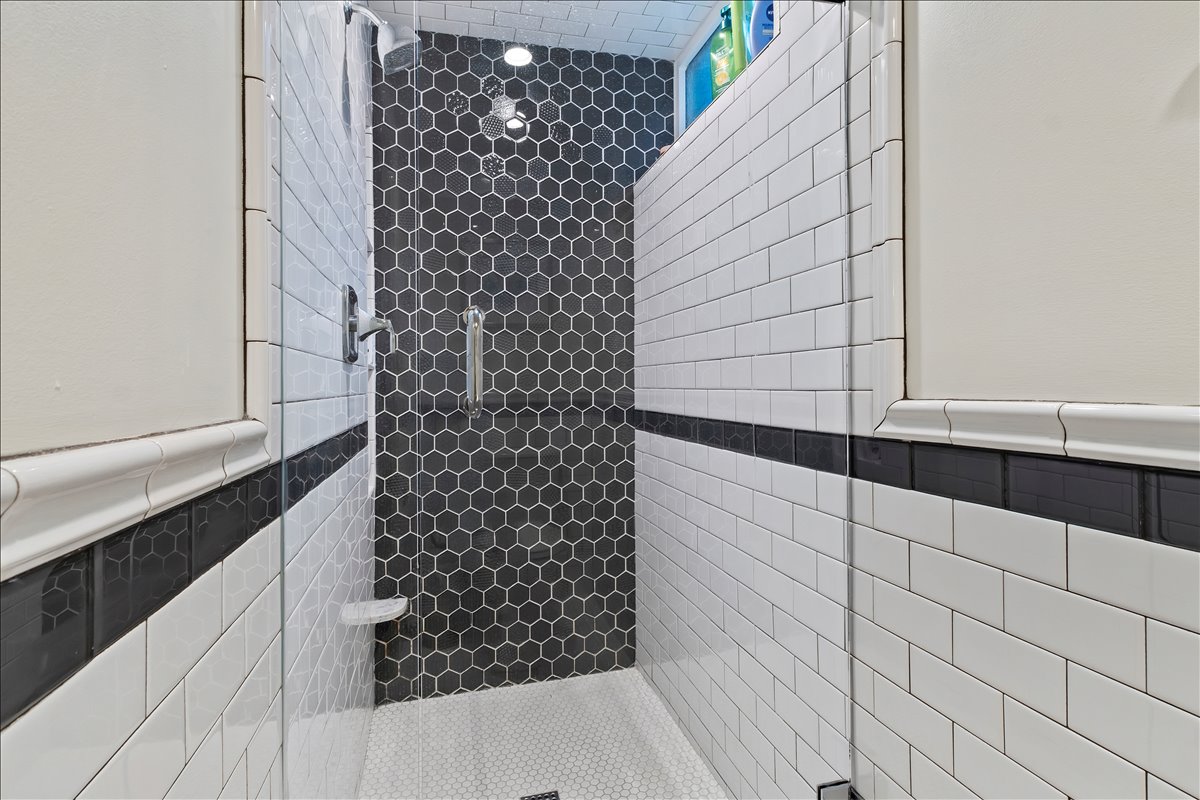 Walk-in shower featuring clear glass enclosure, hexagon tile accent wall, subway tile walls, and a recessed light fixture