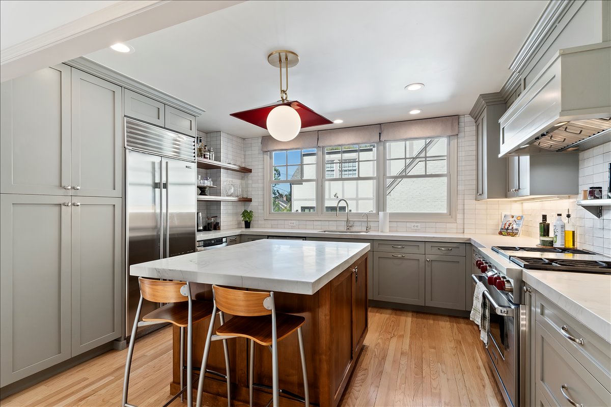 Kitchen featuring an oversized island with countertop seating, light wood-finish flooring, stainless steel appliances, grey cabinetry, and a subway tile backsplash