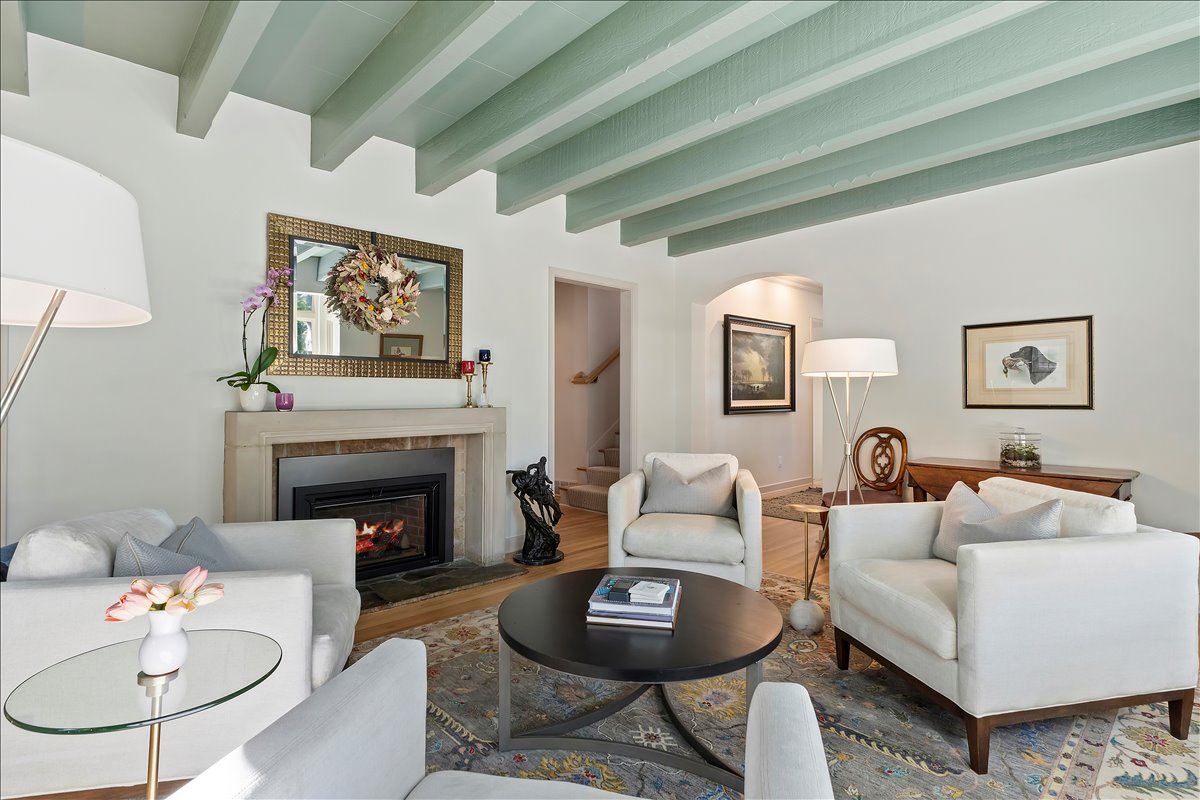 Living area featuring a stone fireplace with a black insert, light wood-finish flooring, and a coffered ceiling with painted beams