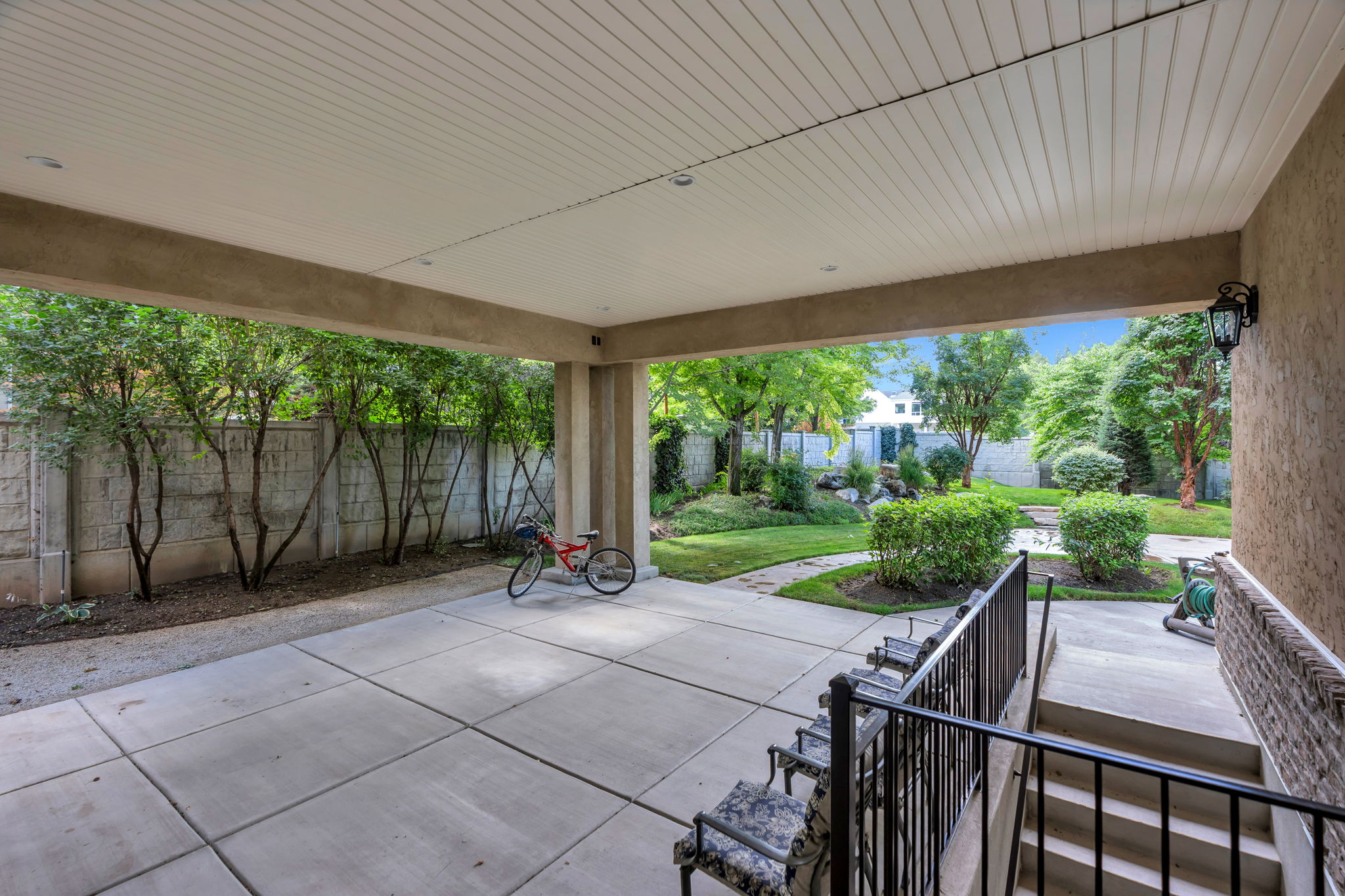 Covered patio with square-paneled concrete flooring, accented by a concrete fence and mature trees