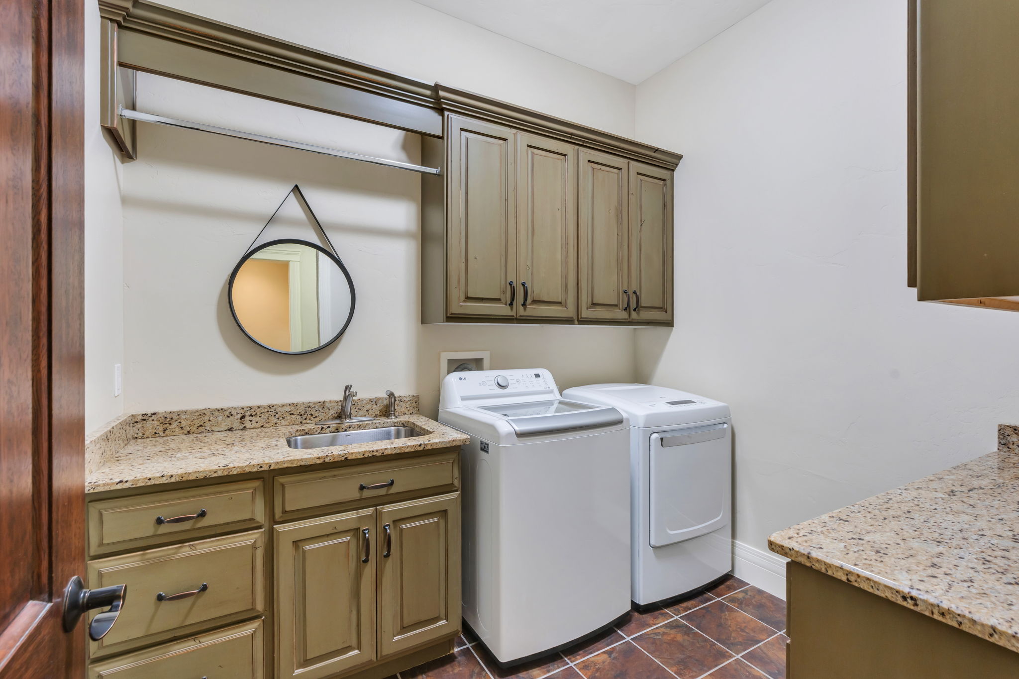 Spacious utility room featuring granite countertops, a stainless steel utility sink, distressed-finish cabinetry, and overhead storage with a hanging rod