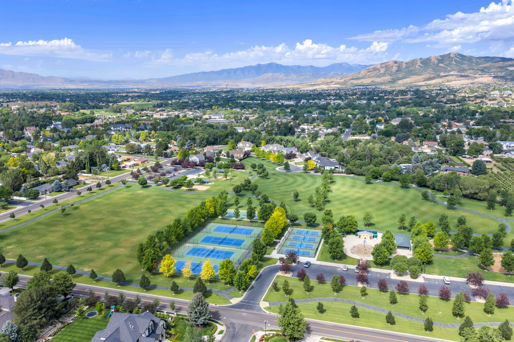 Expansive green spaces featuring Creekside Park with manicured lawns,  tennis & pickleball,  and mature trees, all set against a backdrop of distant mountains