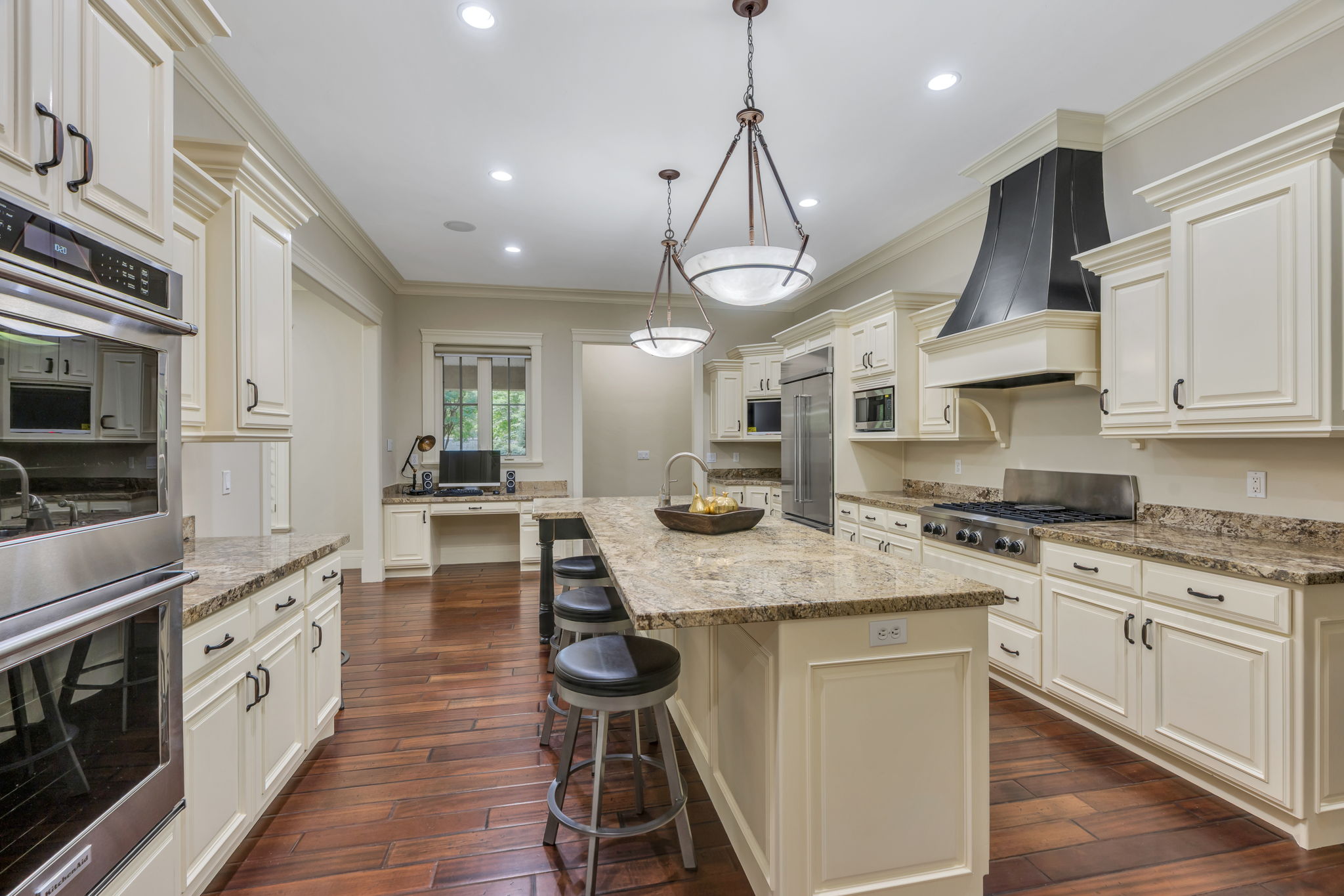 Spacious kitchen featuring an expansive center island with seating, cream-colored cabinetry, stainless steel appliances, granite countertops, and rich wood-finish flooring