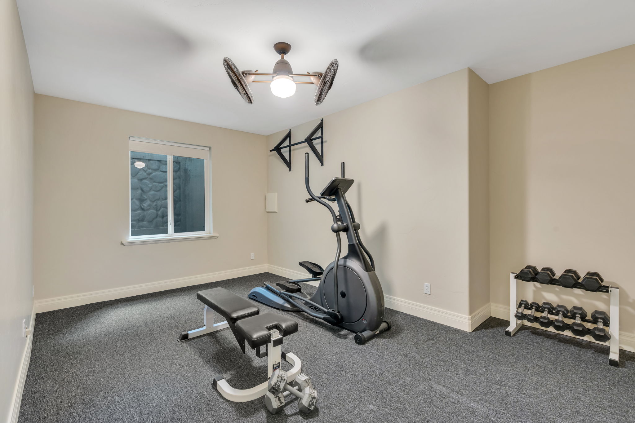 Dedicated fitness room featuring dark textured flooring, a single window, and a ceiling fan with integrated lighting