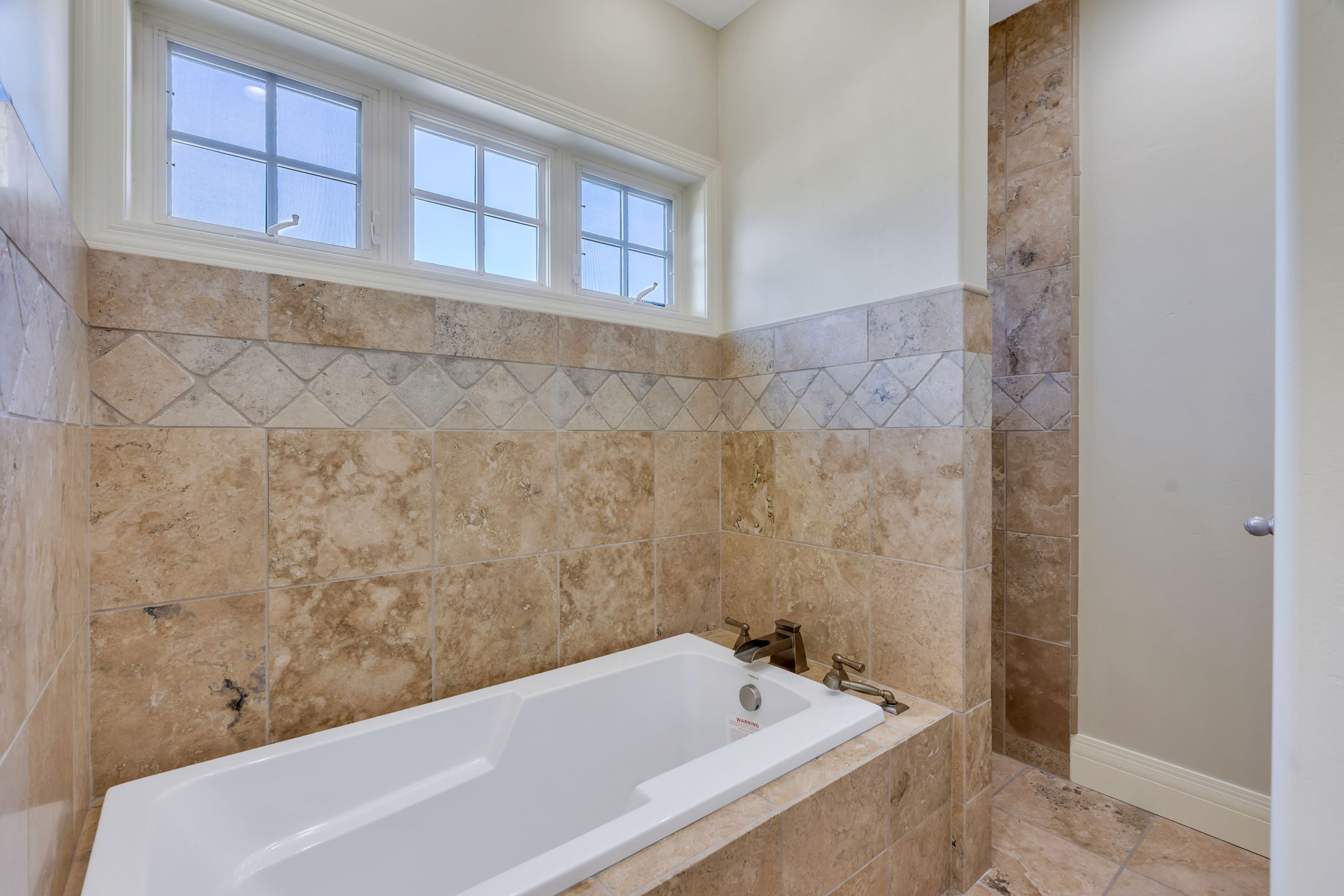New Built-in soaking tub surrounded by natural stone tiling with entrance to doorless shower