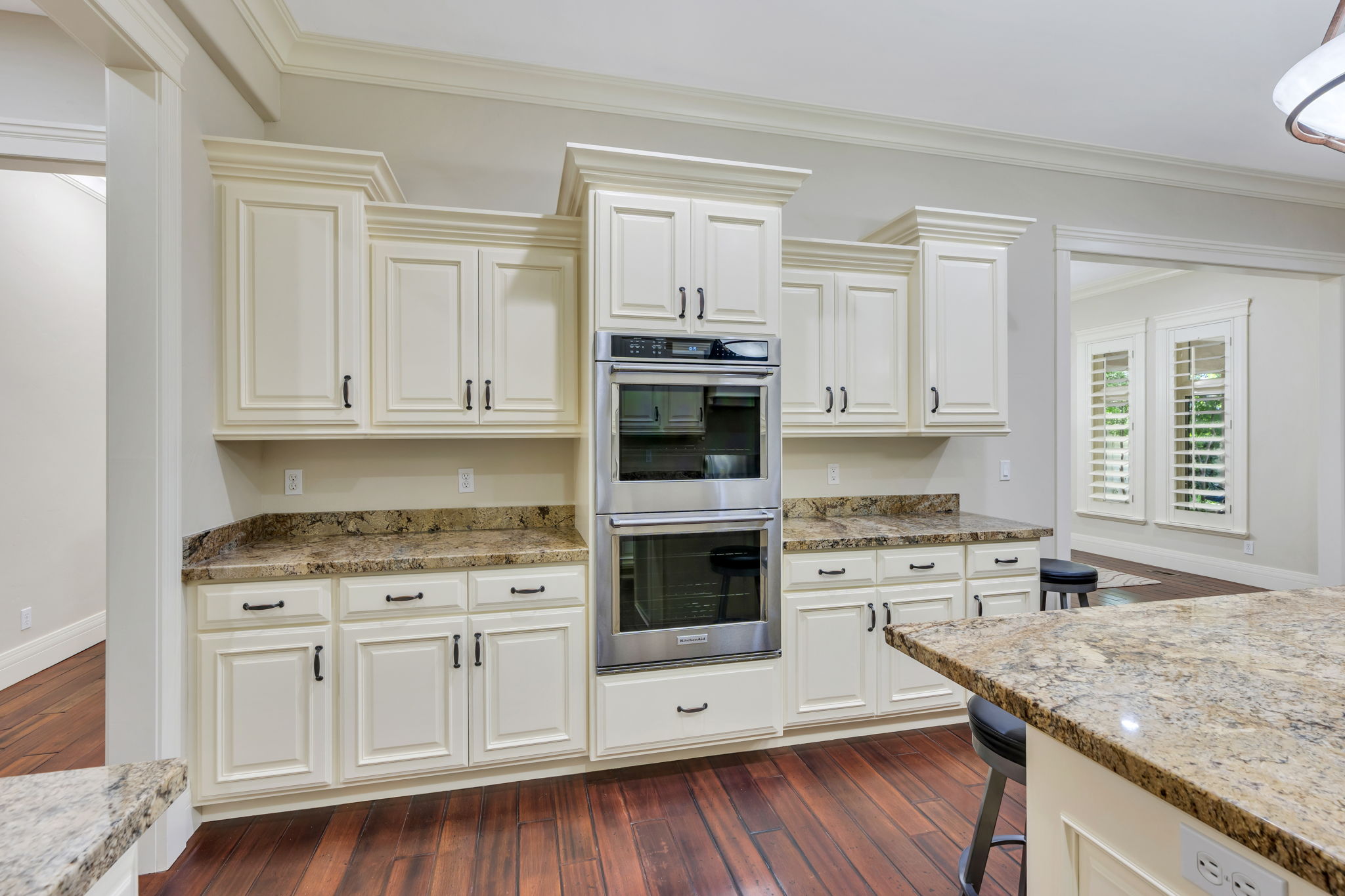 Kitchen featuring cream-colored cabinetry, stainless steel double wall ovens, rich wood-finish flooring, and  granite countertops