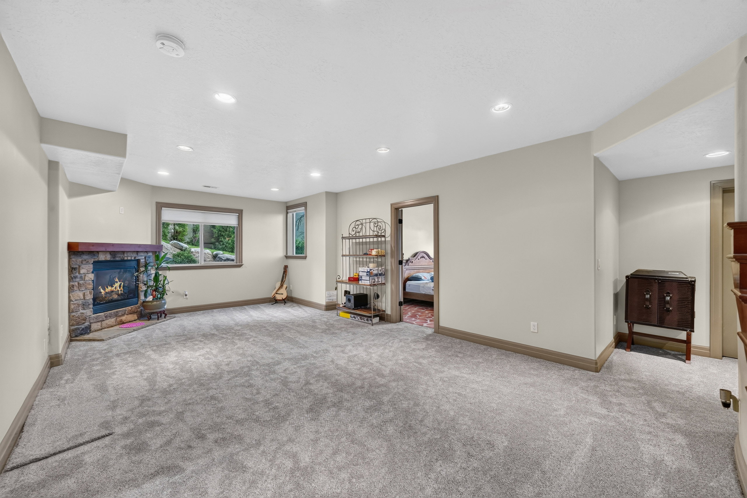 Spacious room featuring plush gray carpeting, a stone-surround fireplace with a wood mantle, and recessed lighting