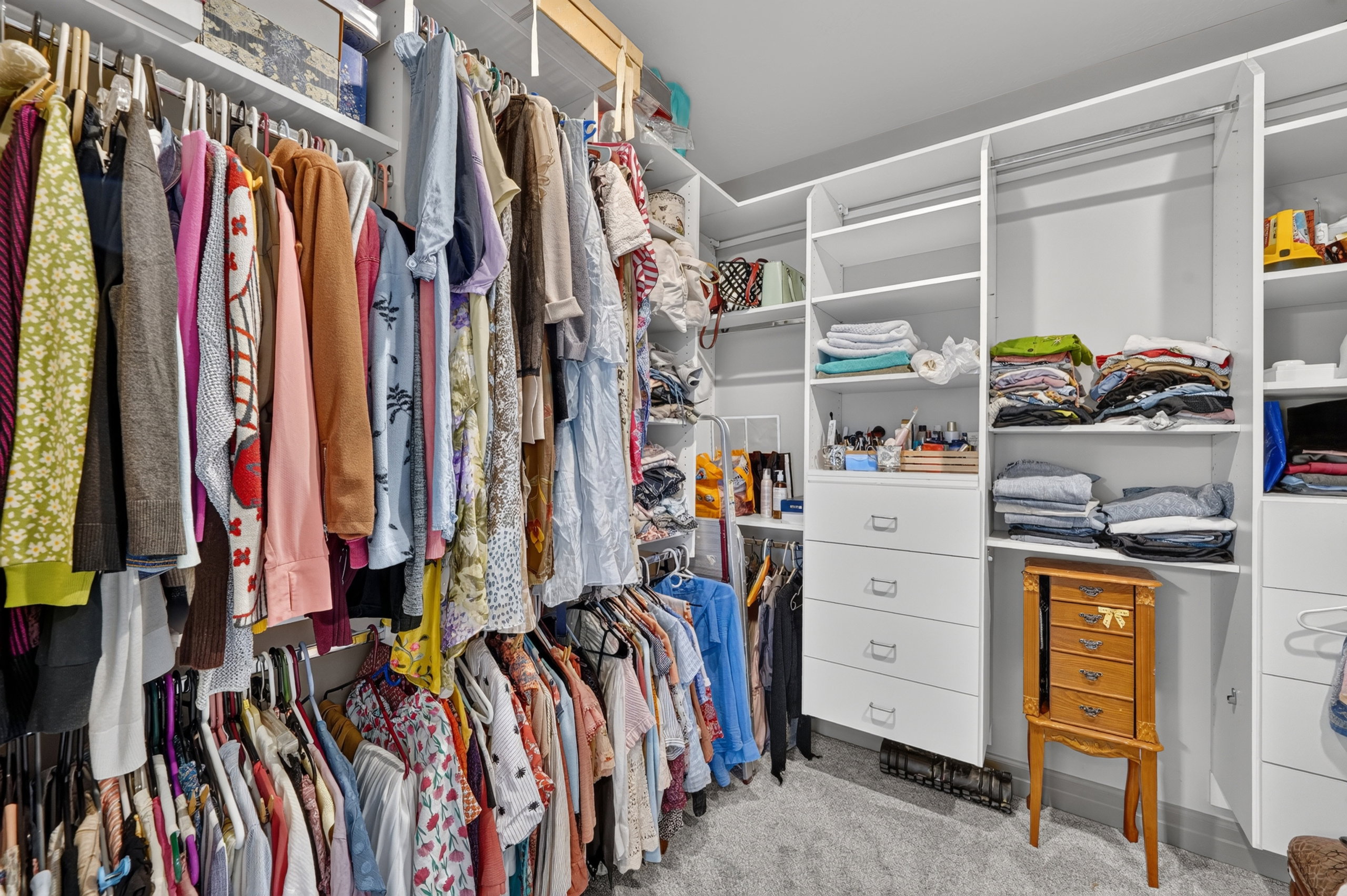 Custom closet system featuring white built-in shelving, multiple hanging rods, and integrated drawers
