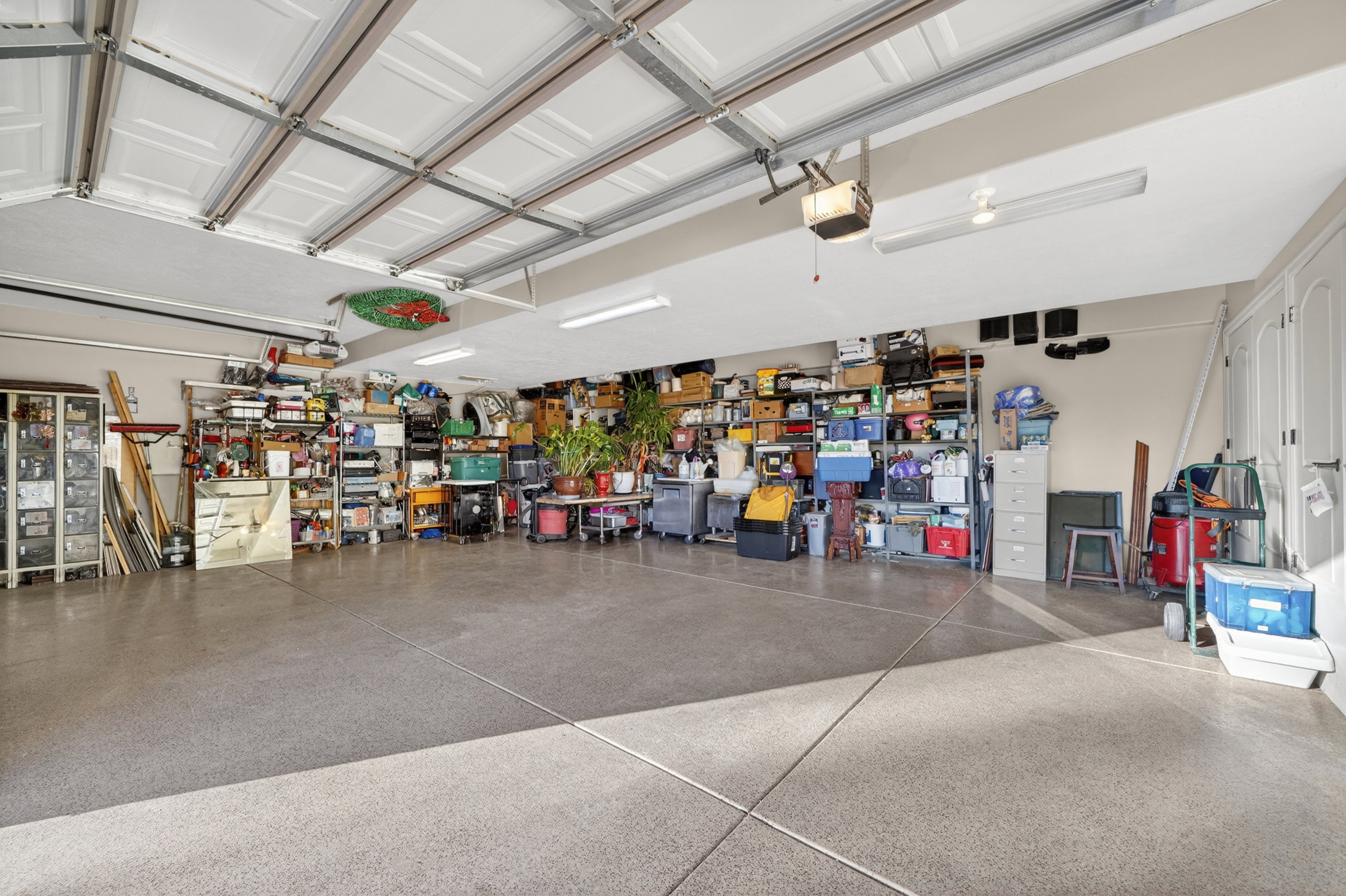 Spacious garage with an epoxy-coated concrete floor, white paneled garage doors, and multiple fluorescent light fixtures