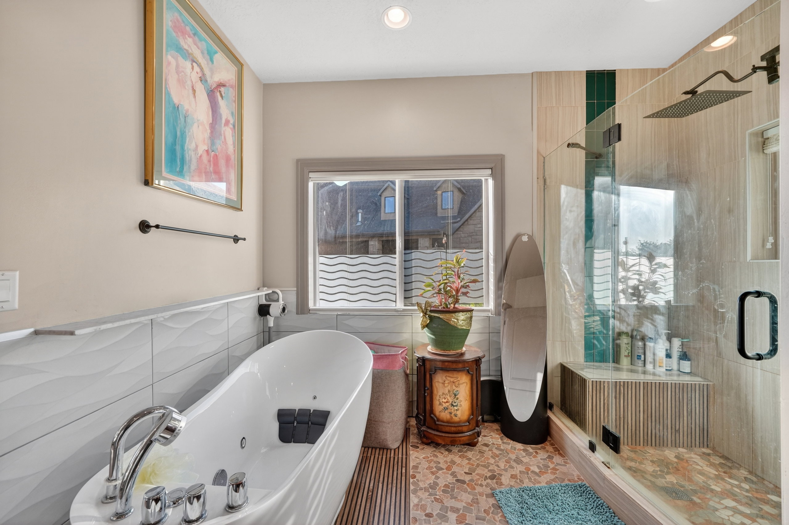 Modern bathroom featuring a freestanding soaking tub with chrome fixtures, a glass-enclosed shower with a rain showerhead, a built-in shower bench, and mixed tile flooring