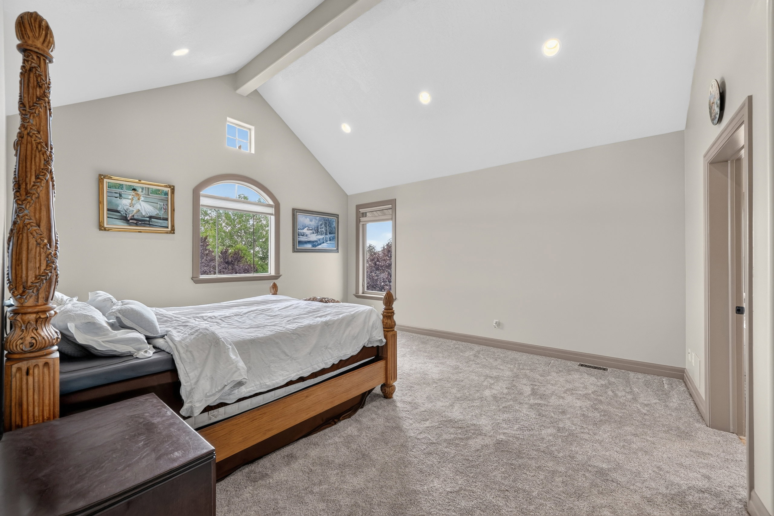Spacious room featuring vaulted ceilings with exposed beam, recessed lighting, arched window, and plush carpet flooring