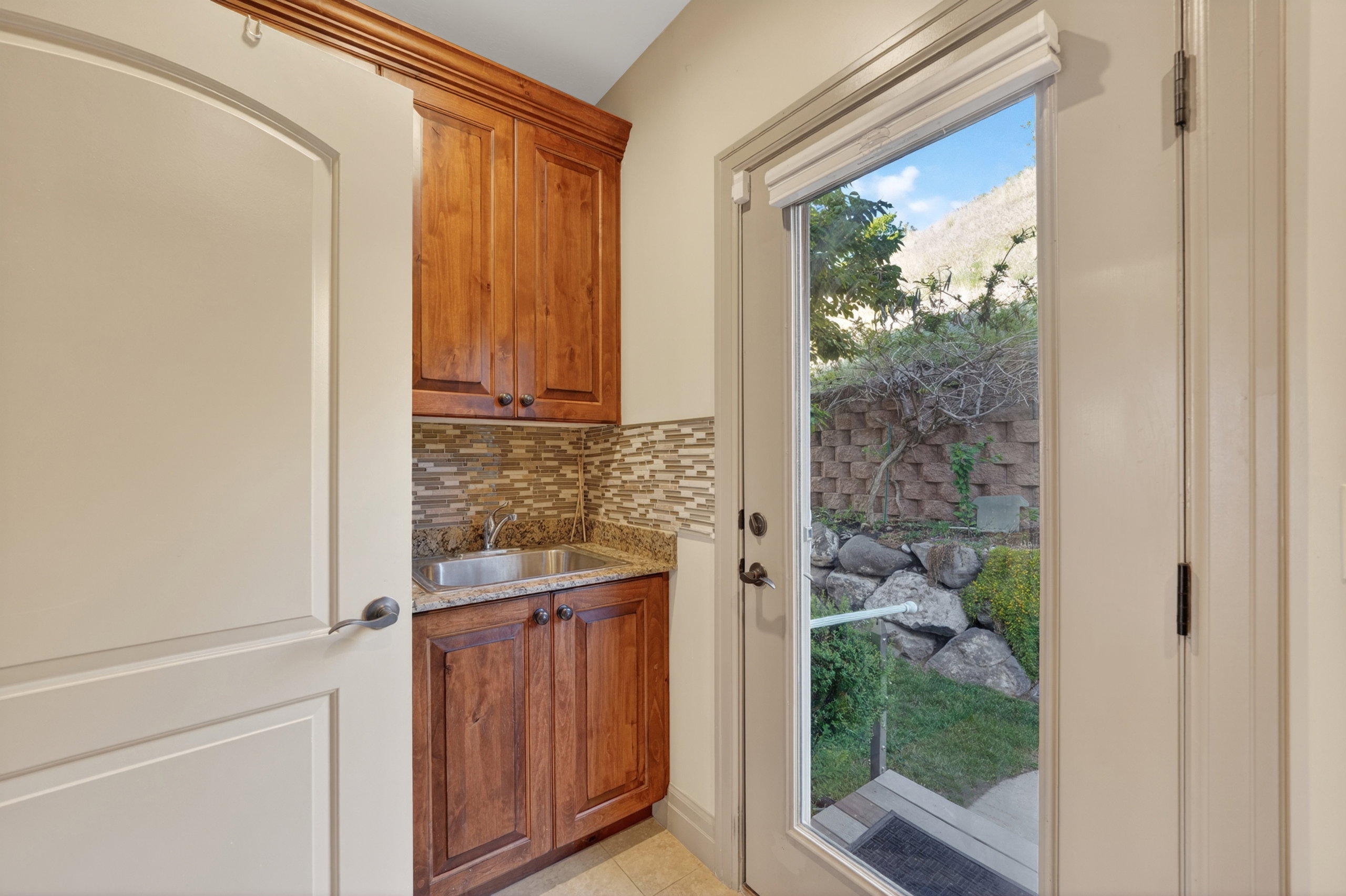 Utility sink area featuring wood-finish cabinetry, a granite-finish countertop, and a mosaic tile backsplash