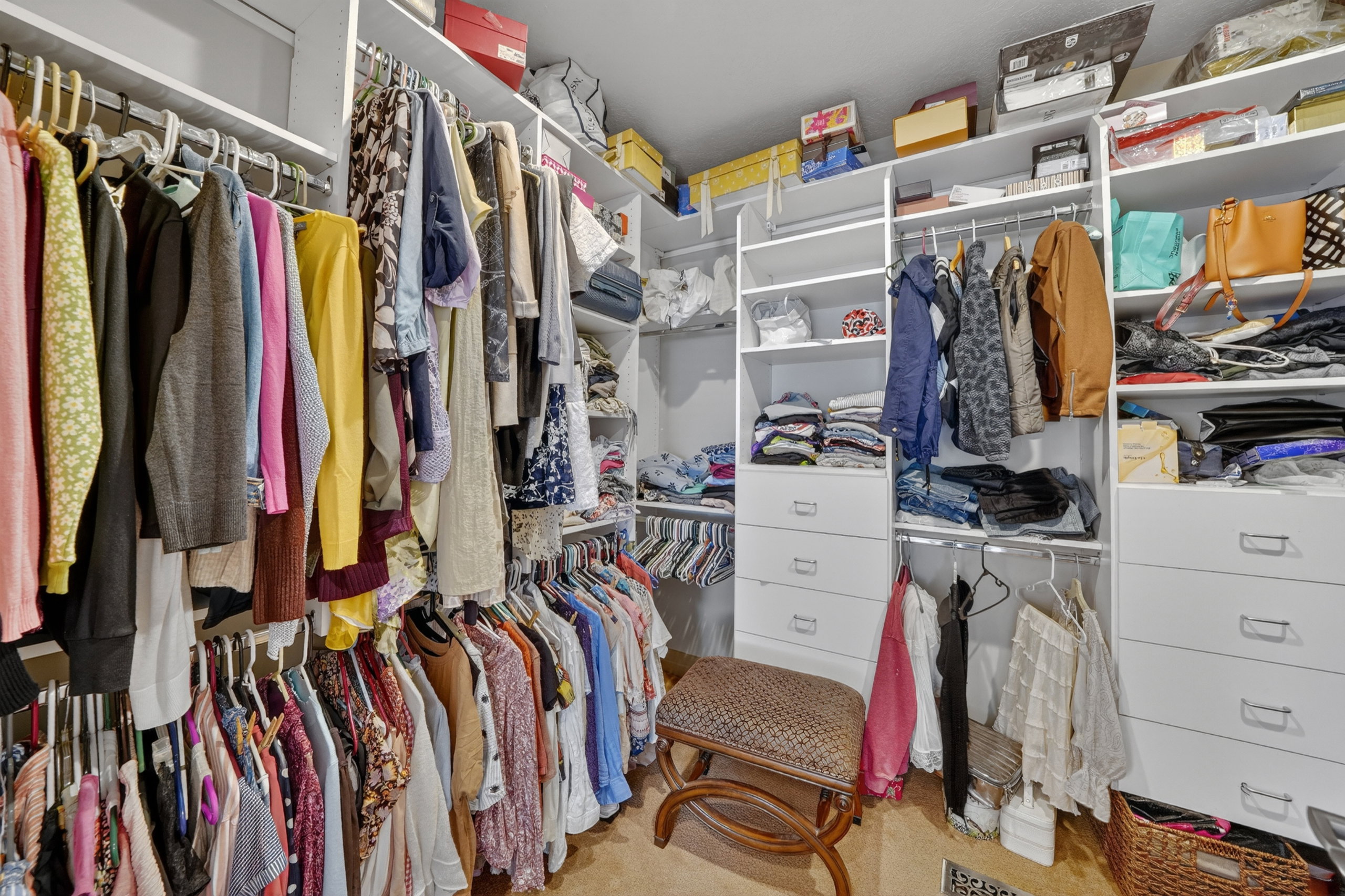 Walk-in closet featuring extensive custom white shelving, multiple hanging rods, built-in drawer storage, and carpet flooring