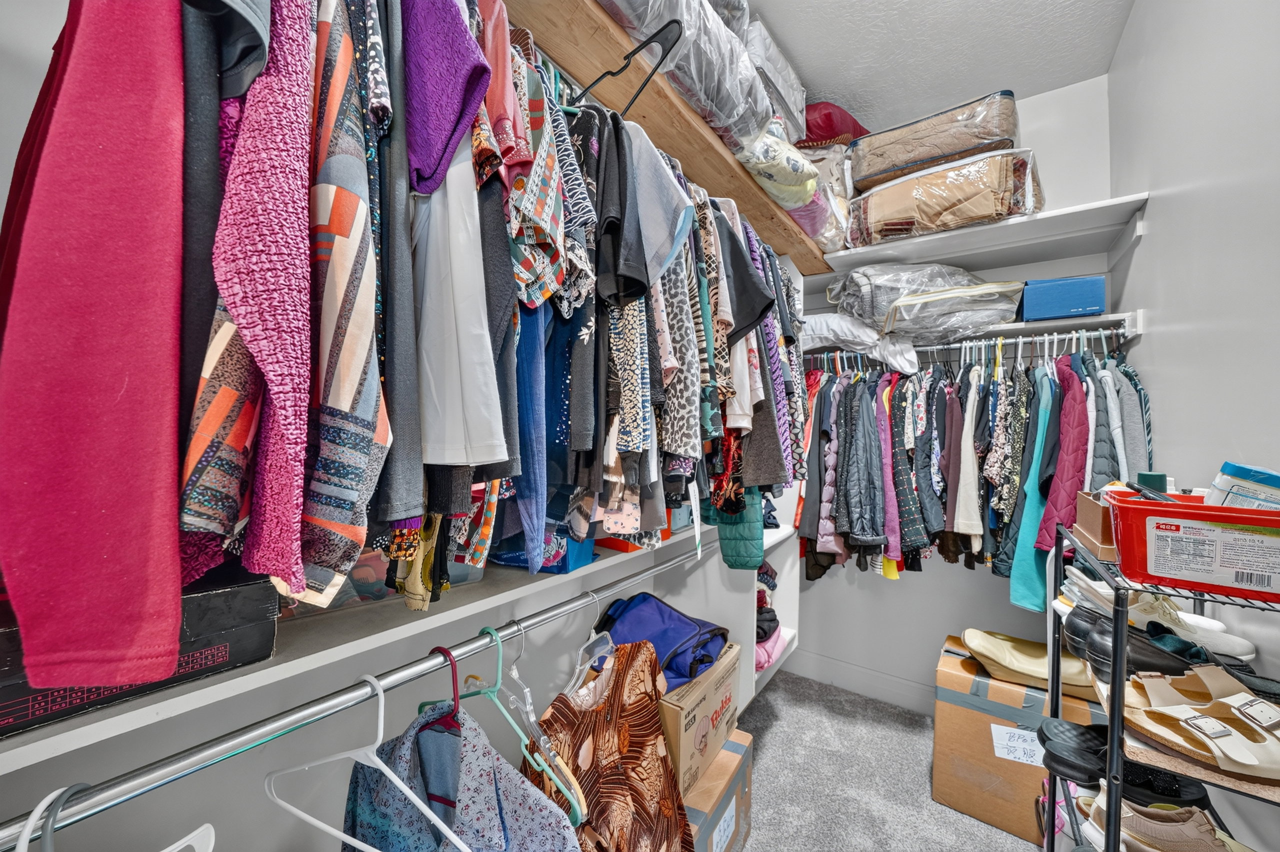 Walk-in closet featuring built-in shelving, multiple hanging rods, and grey carpeting