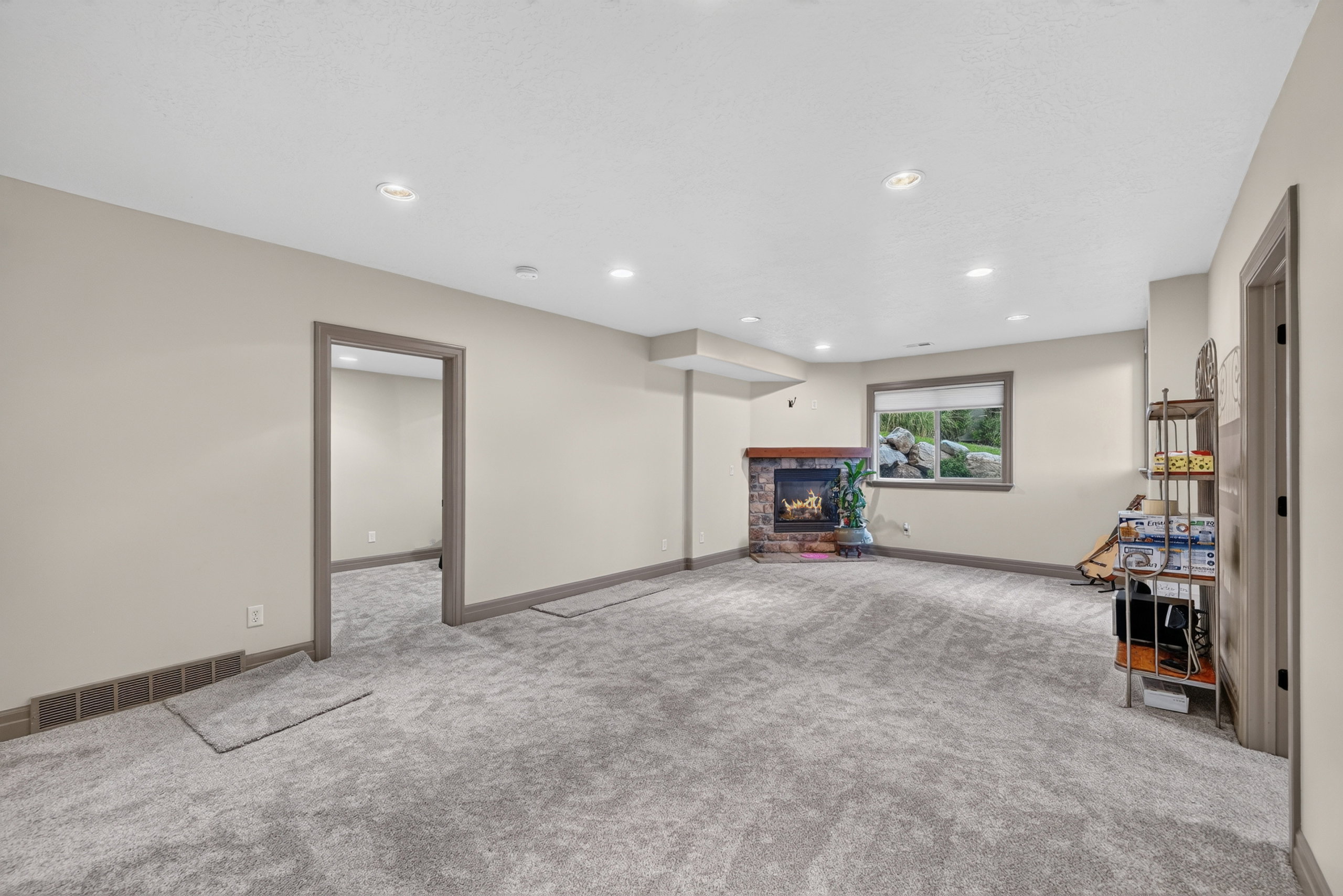 Spacious carpeted room featuring a stone-faced fireplace with a wood mantel, recessed lighting, and a window providing natural light