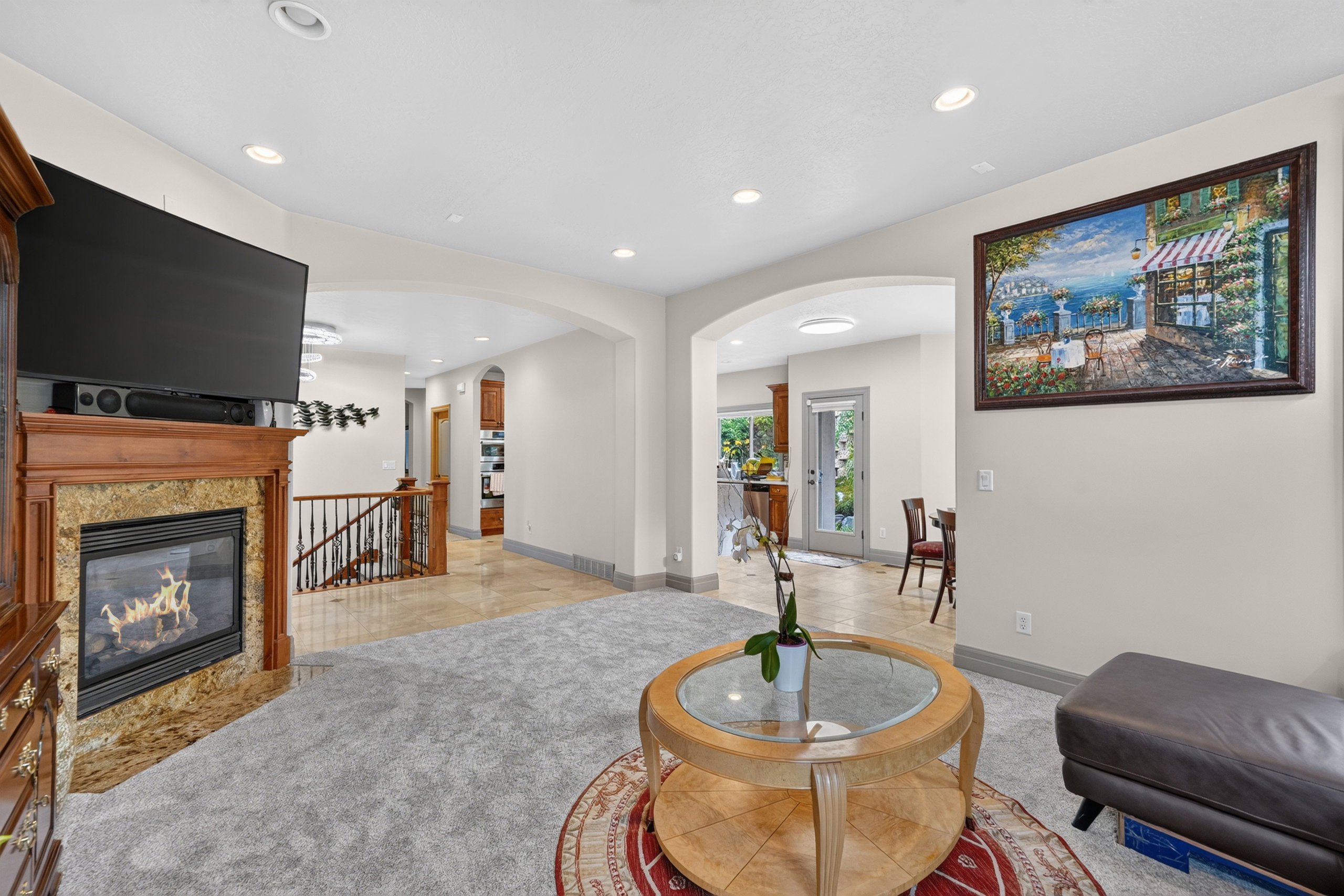 Living area featuring a stone-surround fireplace with wood mantel, light-toned carpeting, recessed lighting, and arched doorways