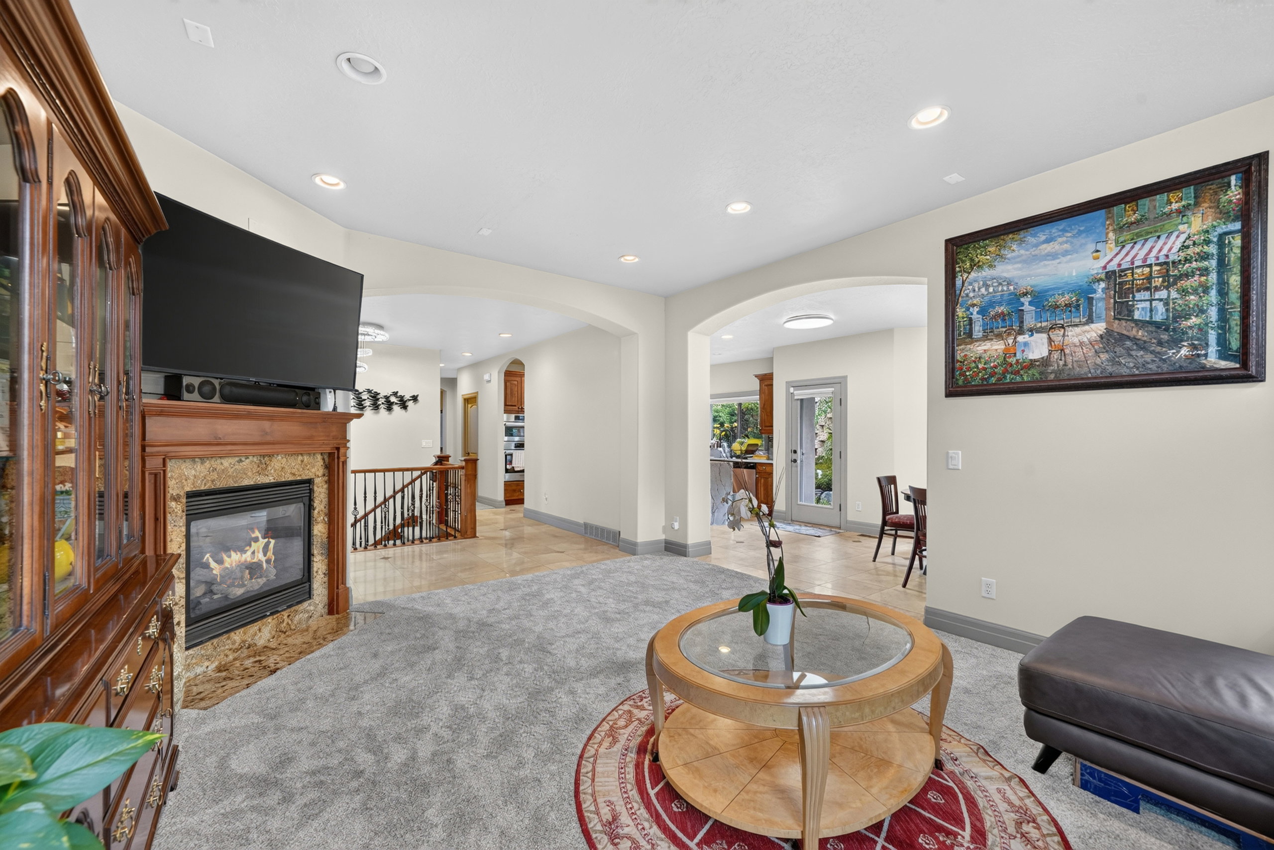 Living area featuring a gas fireplace with a stone surround, recessed lighting, arched doorways, and light gray carpeting