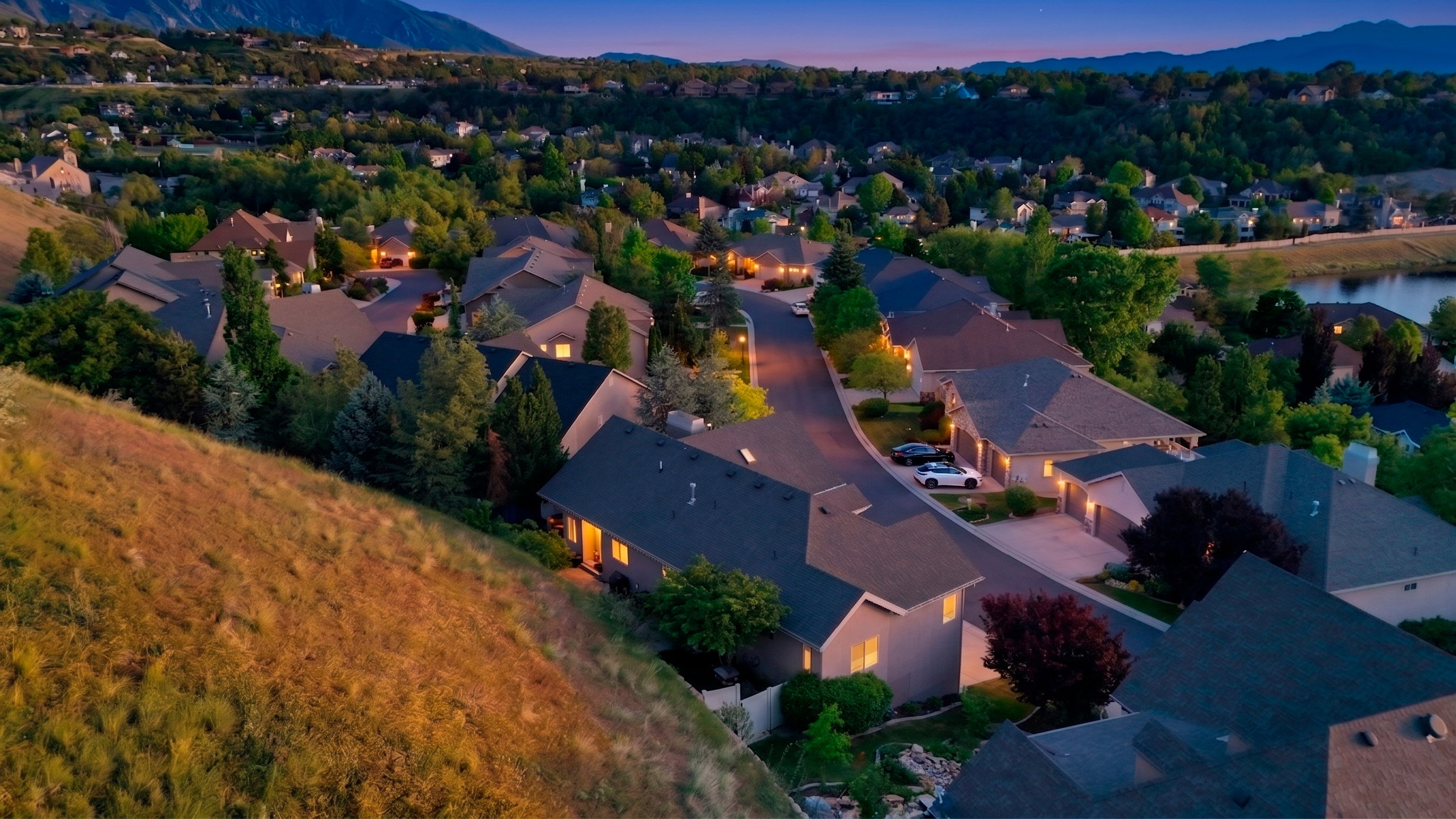Residential street featuring varied rooflines, mature trees, a distant body of water, and mountain scenery