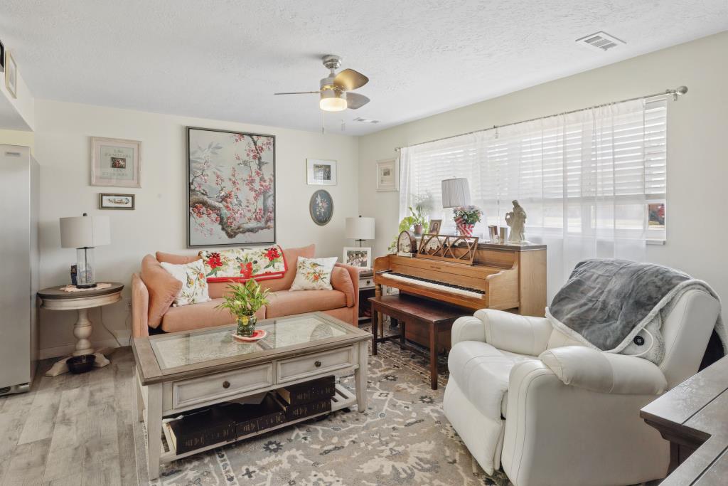 Spacious living area featuring light-toned walls, wood-finish flooring, and a ceiling fan with integrated lighting