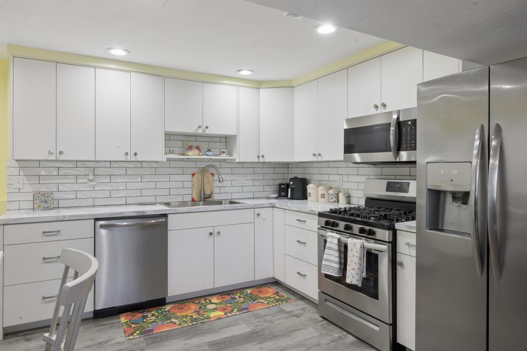 Modern kitchen featuring white cabinetry, subway tile backsplash, stainless steel appliances, and a double basin sink