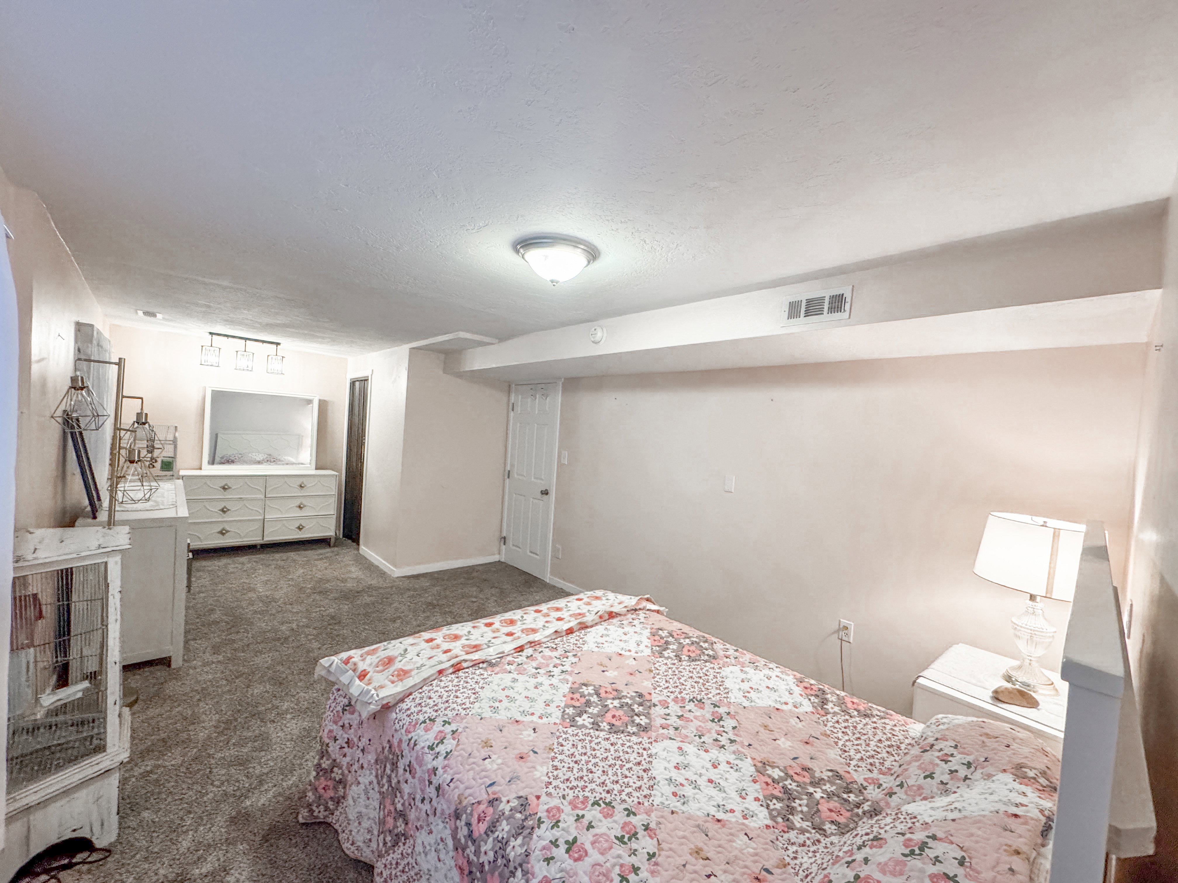 Carpeted interior space featuring a flush-mount ceiling light fixture, wall-mounted vent, white interior door, and a light-colored wall finish