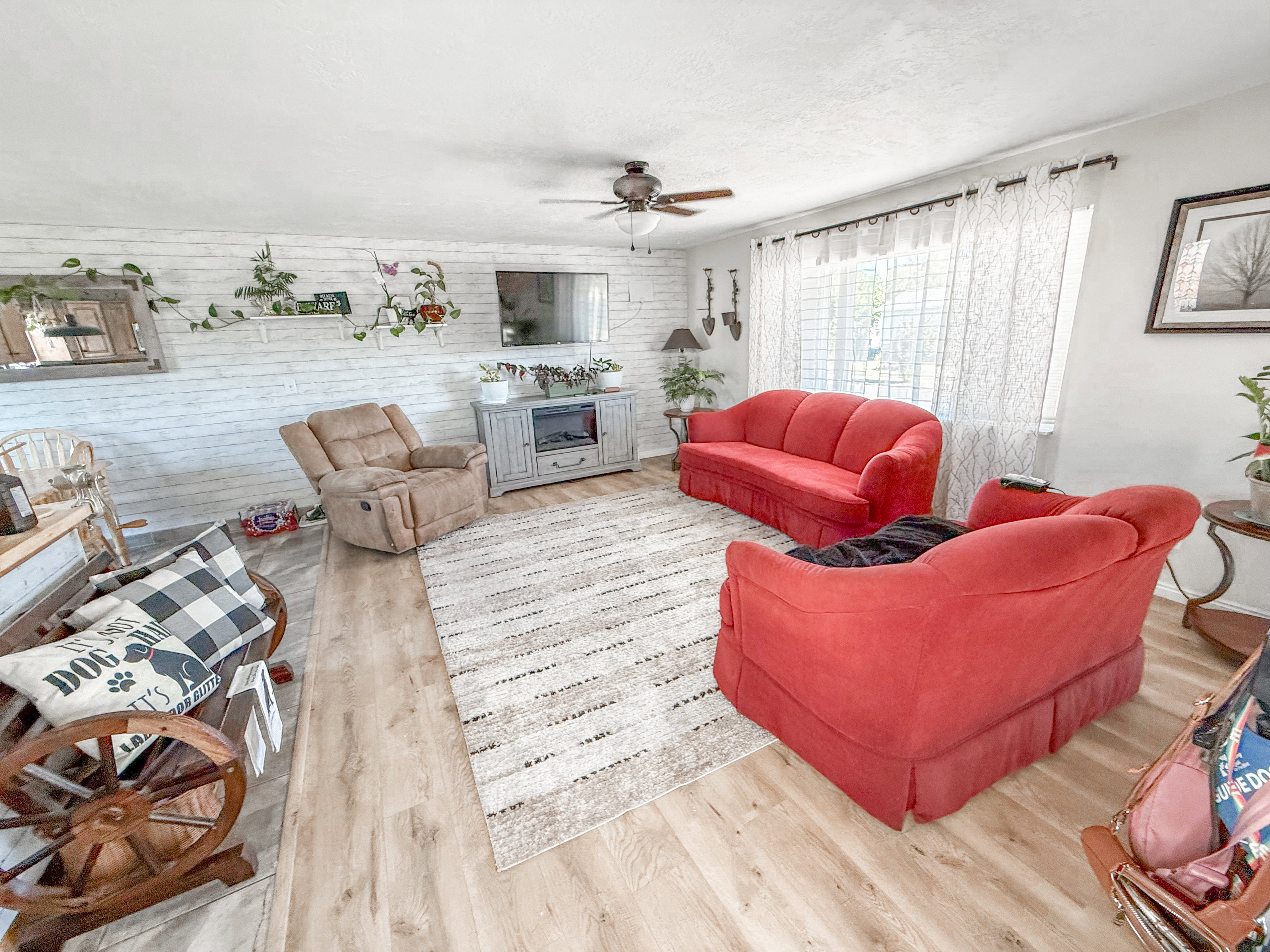 Living area featuring light wood-finish flooring, a ceiling fan with integrated lighting, and a prominent shiplap accent wall