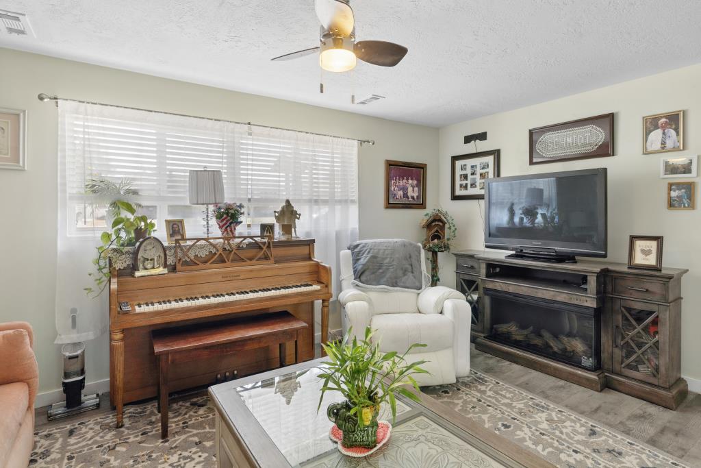 Living area featuring light-toned walls, ceiling fan with integrated lighting, and a window with horizontal blinds