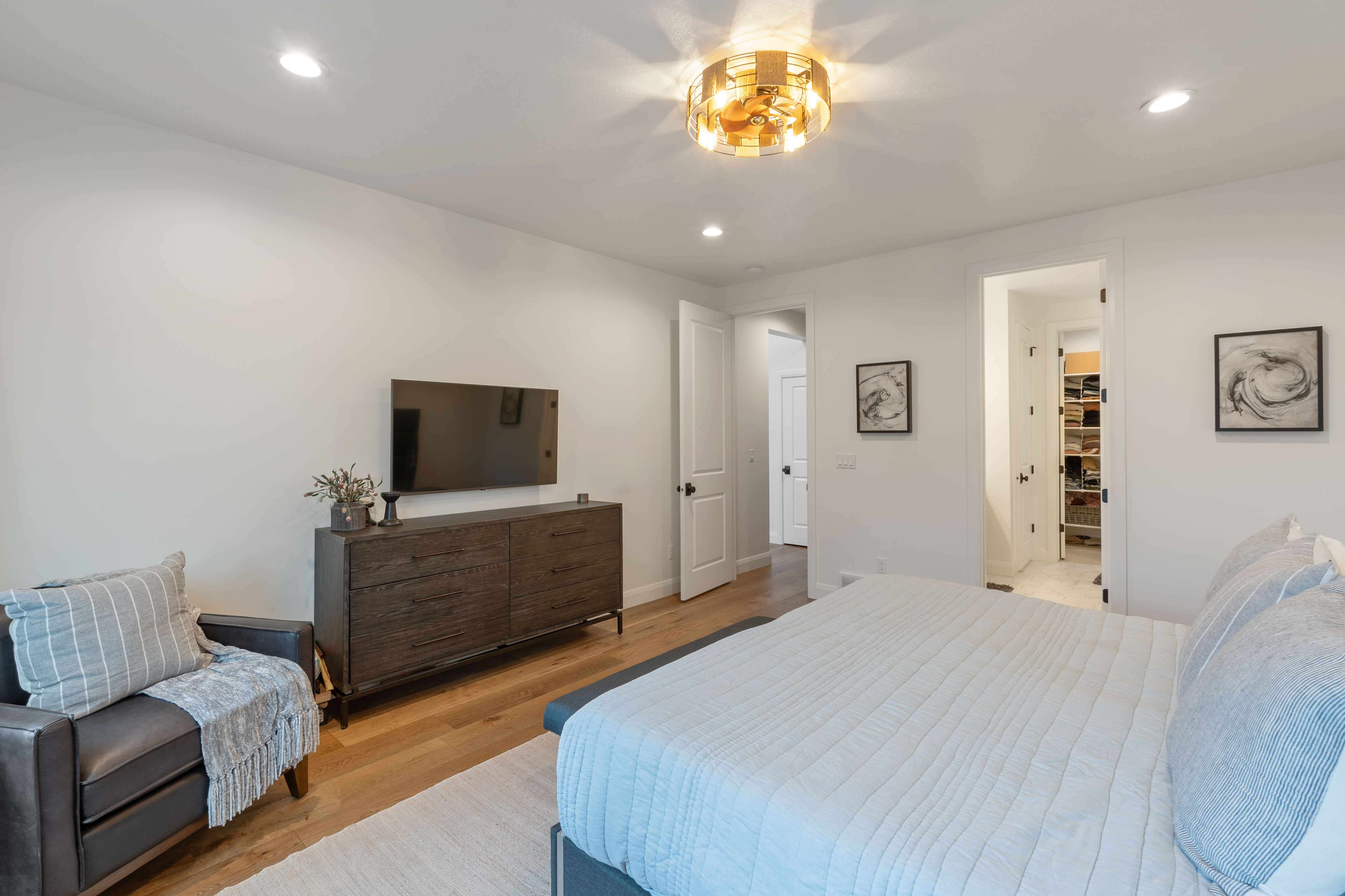 Master on Main - Interior room featuring light wood-finish flooring, white walls, and a contemporary gold-finish ceiling light fixture